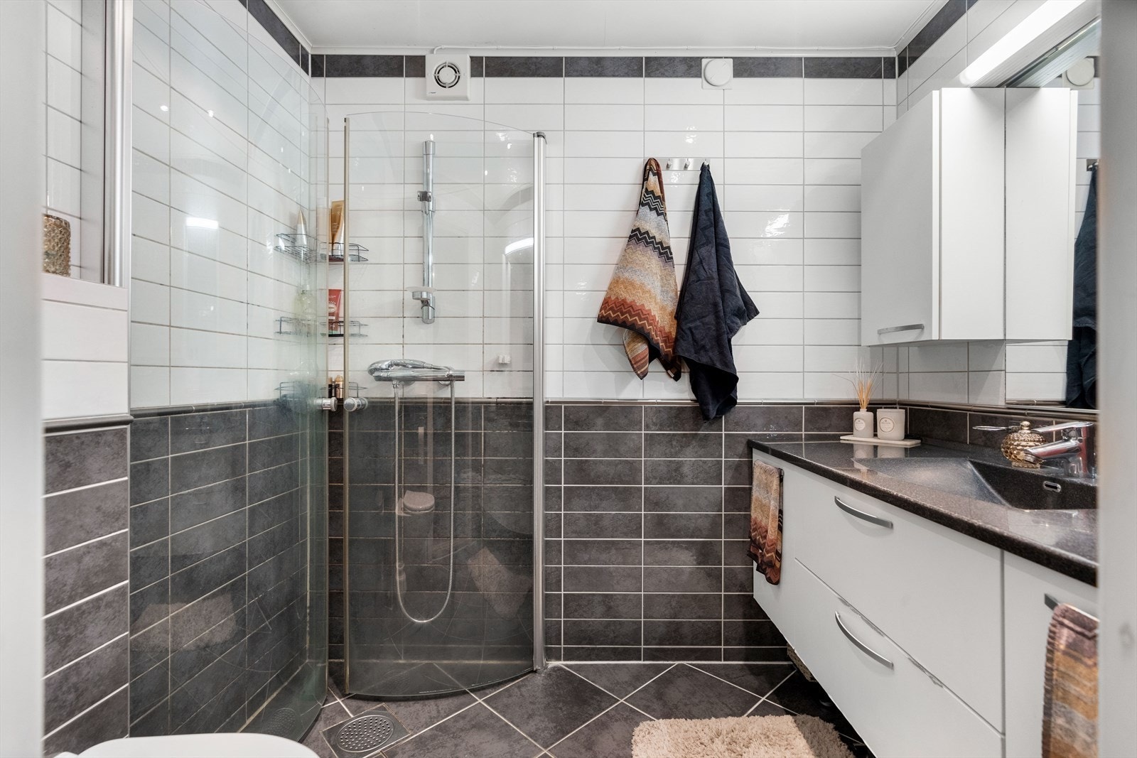 Tidløst baderom med vegghengt servantinnredning, dusjhjørne med innfellbare glassdører og vegghengt toalett. Galleribilde