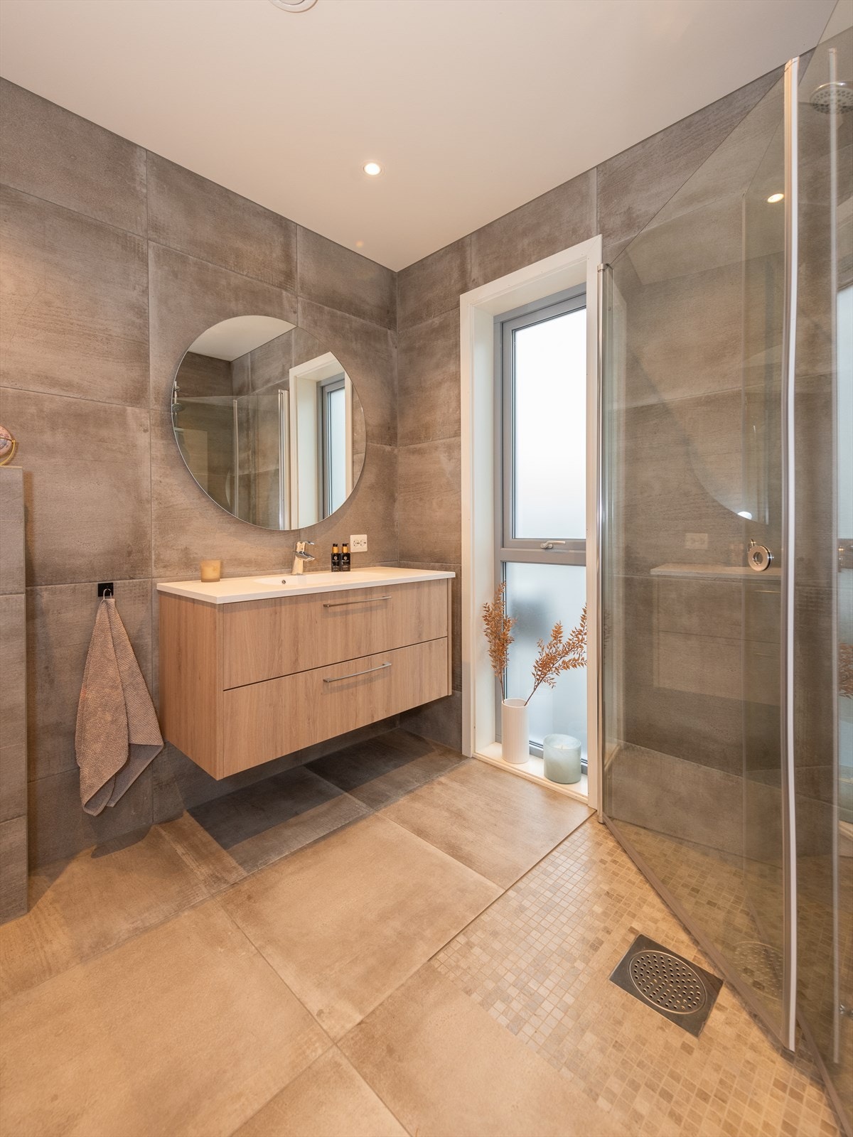 Det har innfelte downlights i himlingen og badet er innredet med vegghengt toalett, dusjhjørne og servant i baderomsinnredning. Badet har varmekabler i gulv. Galleribilde