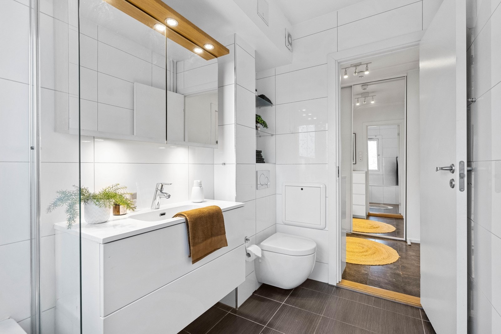 Badet er i moderne og tidløs stil og er utstyrt med nedfelt servant, vegghengt toalett, i tillegg til et innmurt og flislagt badekar med dusjarmatur. Galleribilde