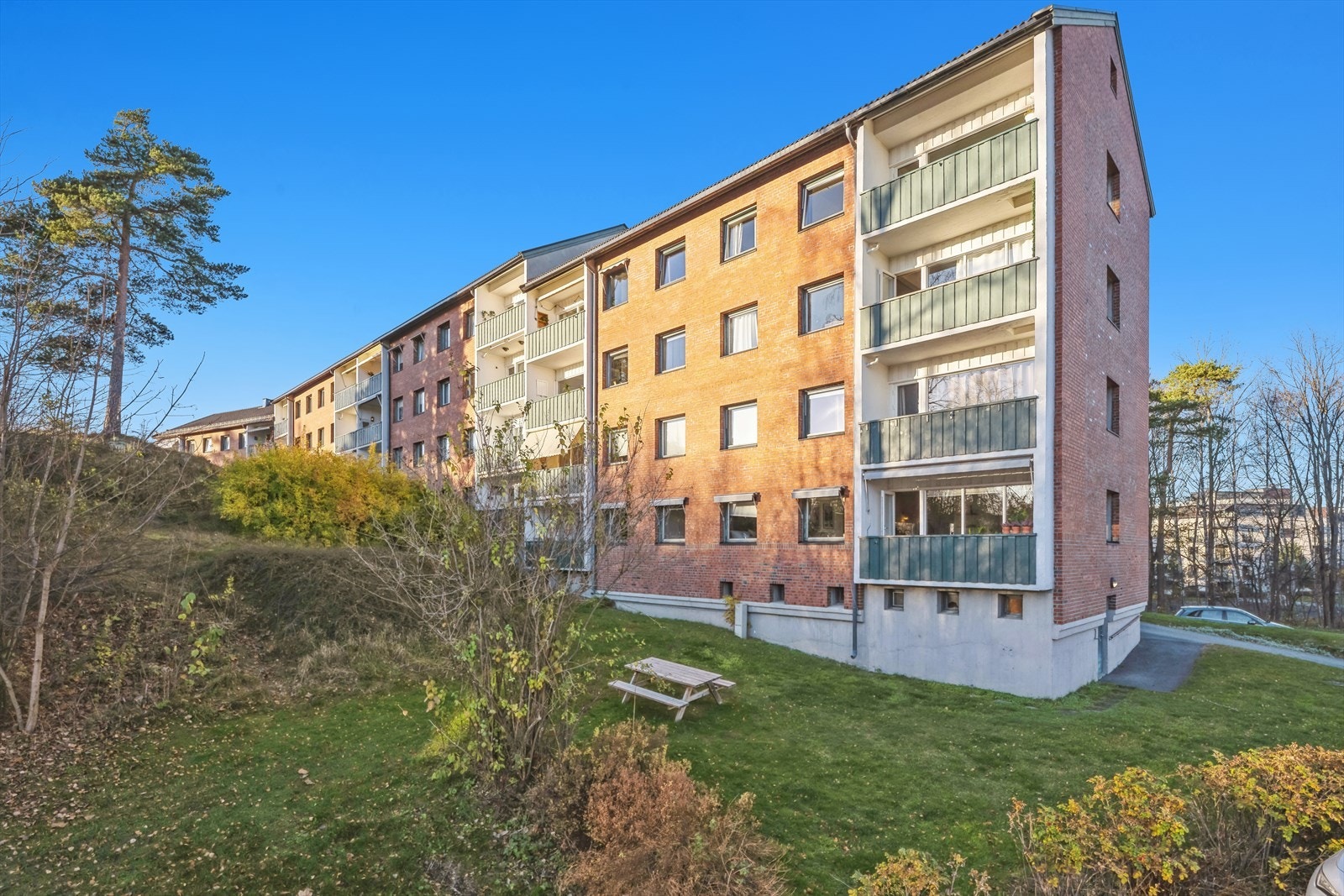 Sameiets grønne fellesarealer utenfor leiligheten. Rett under leiligheten, grønn dør på enden av bygget, ligger sameiets felles sykkelbod. Galleribilde