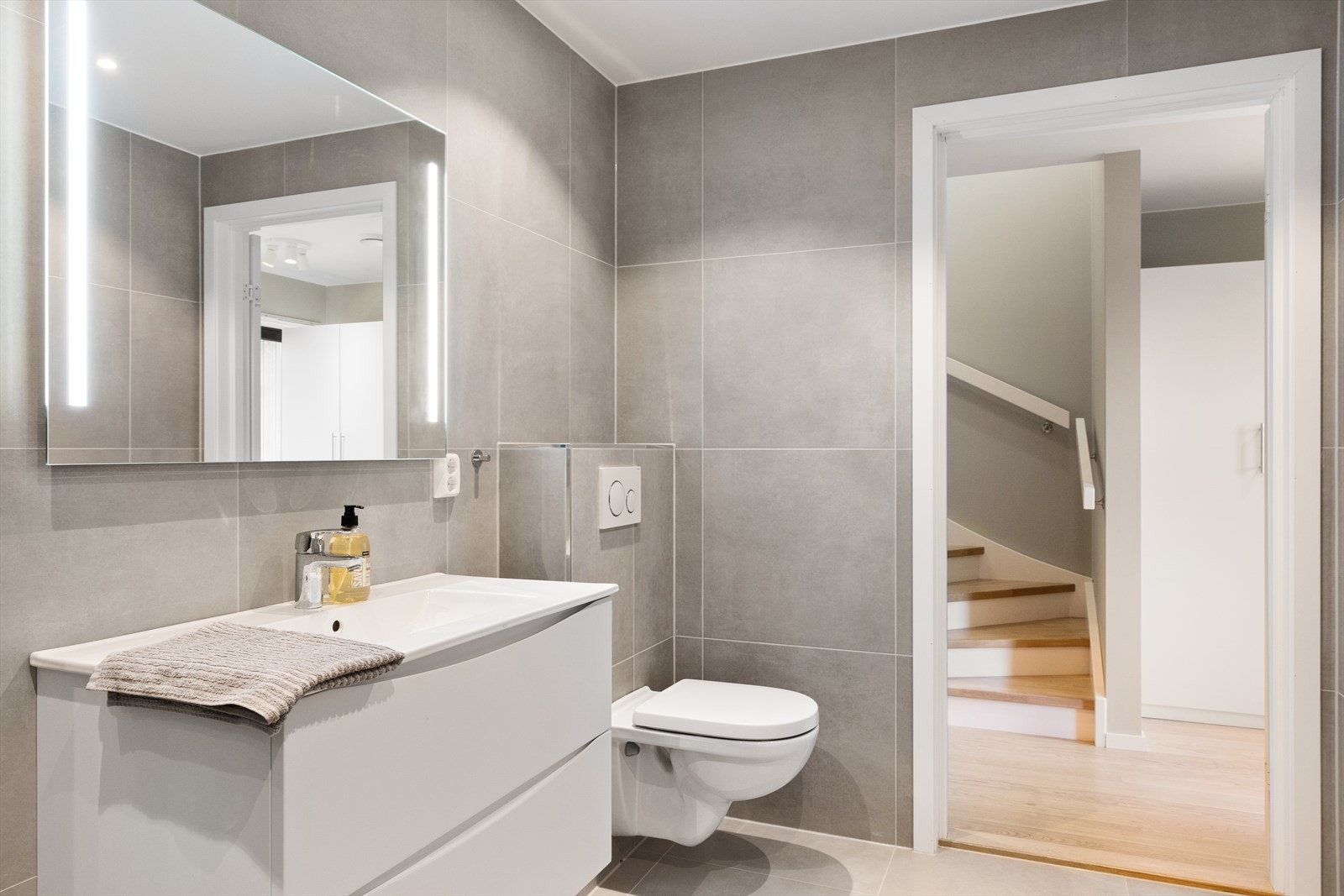 Badet er innredet med vegghengt toalett, servant integrert i en moderne innredning, speilskap med belysning og et praktisk dusjhjørne med svingbare glassdører. Galleribilde