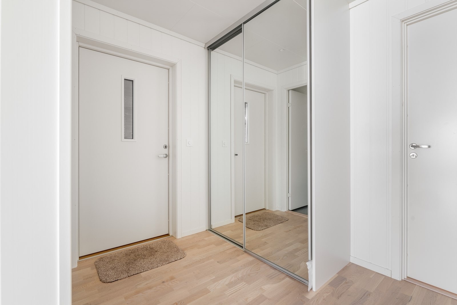 Lys og fin entré ønsker deg velkommen inn i boligen. Her er det parkett på gulv, og hvitmalte vegger og himling som er gjennomgående i hele boligen og gir en fin helhet. Praktisk skyvedørsgarderobe med speilfronter like på innsiden av døren. Galleribilde