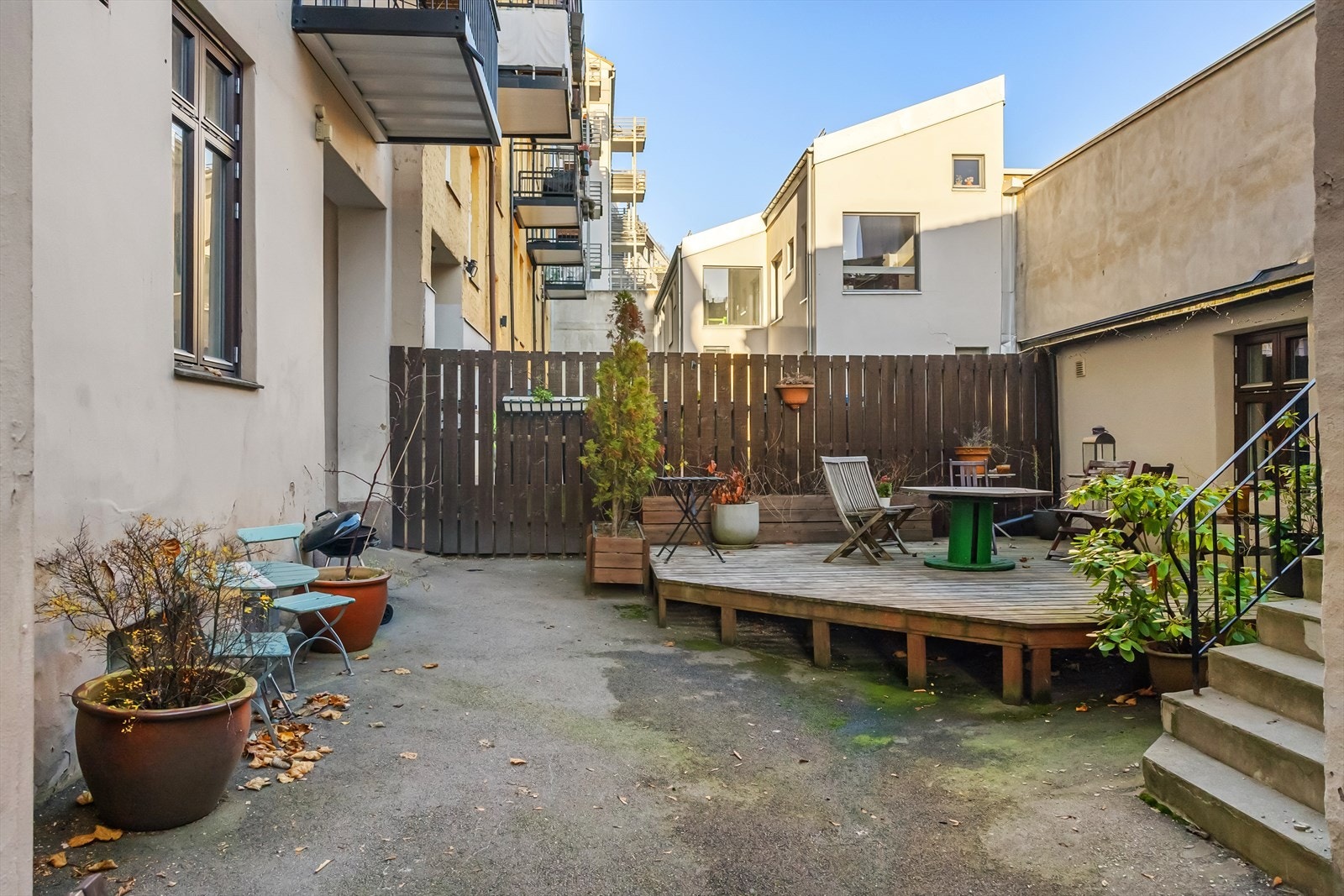 Lukket bakgård med asfalt. Her er det platting med flere sittegrupper, grill og beplanting. Galleribilde