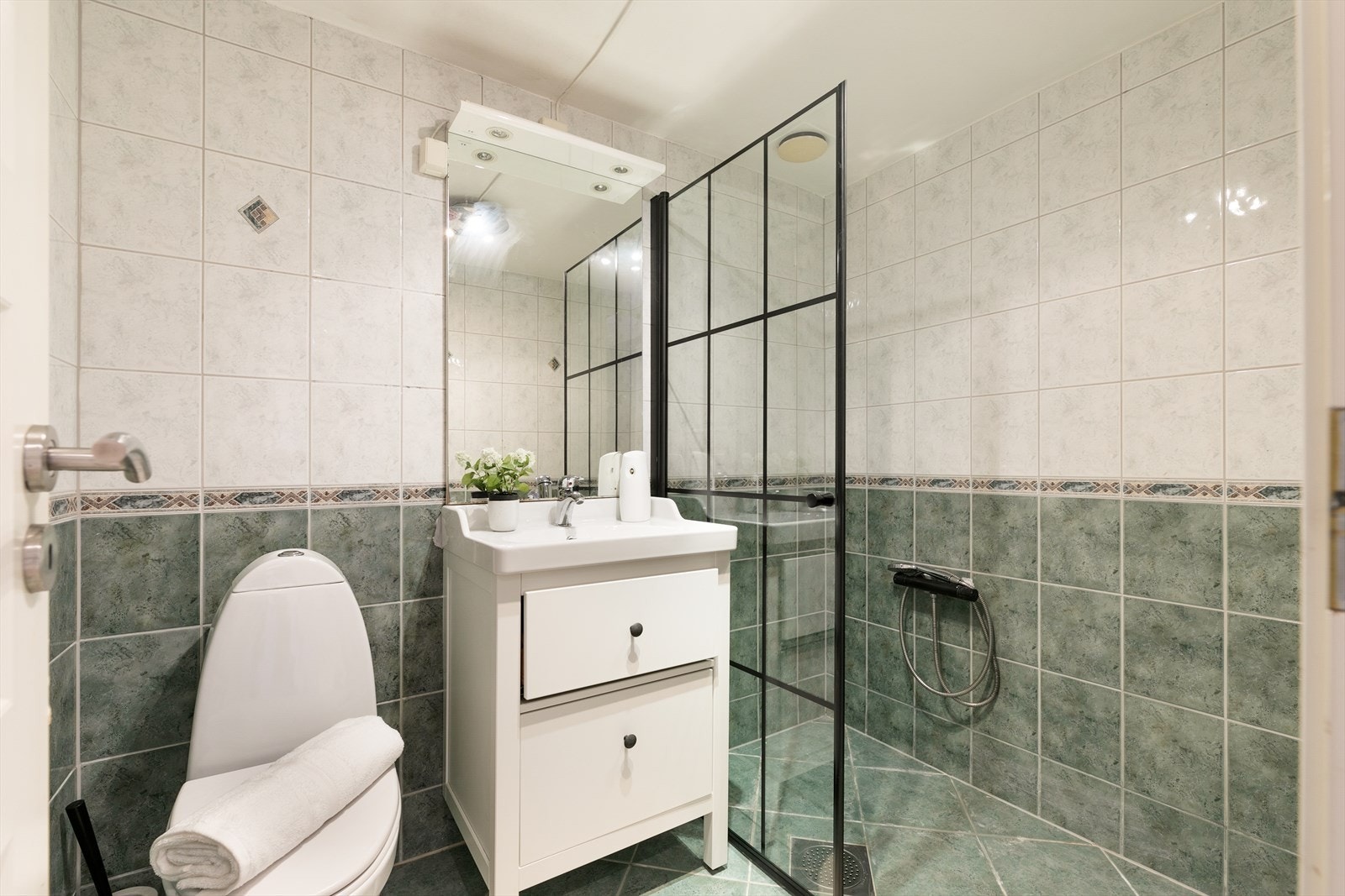 Flislagt bad/wc med varmekabler i gulv, servant med skuffer, toalett, og dusj med skillevegg i glass Galleribilde