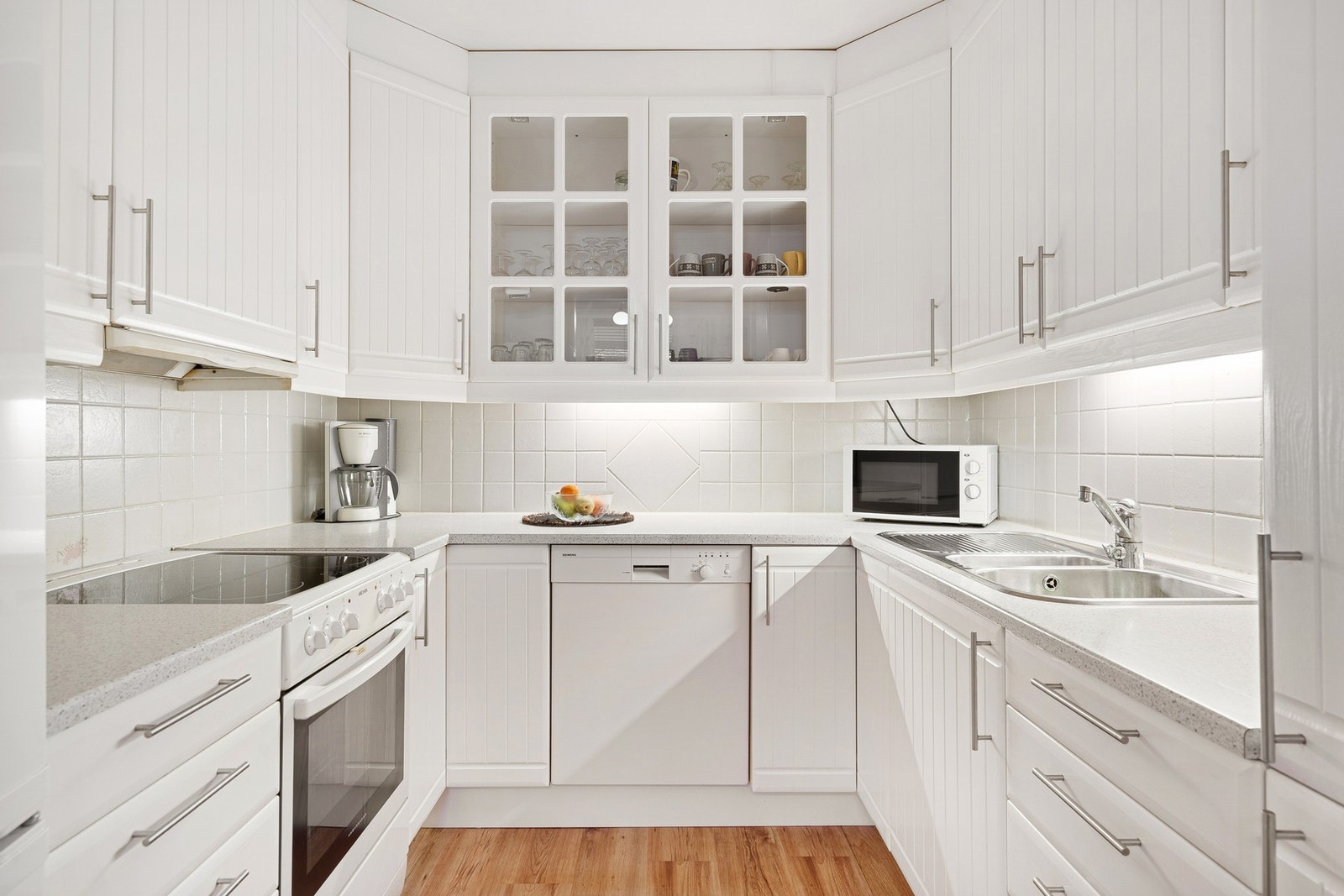 Kjøkkenet er utstyrt med flis over benkeplate, lys i glasskap og rikelig med skap- og benkeplass. Galleribilde