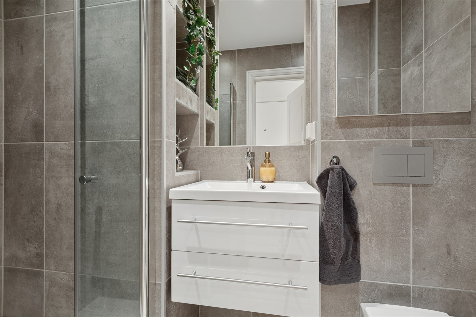 Delikat flislagt bad fra 2017 med varmekabler i gulv. Innredningen består av servant med underskap, speil, dusjhjørne med glassdører og vegghengt toalett. Galleribilde