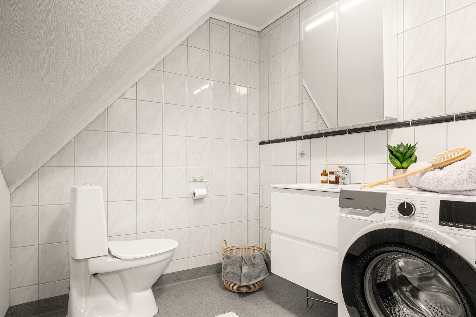 Rommet måler 4,4 kvm og er innredet med dusjkabinett, toalett, baderomsinnredning og opplegg for vaskemaskin. Galleribilde