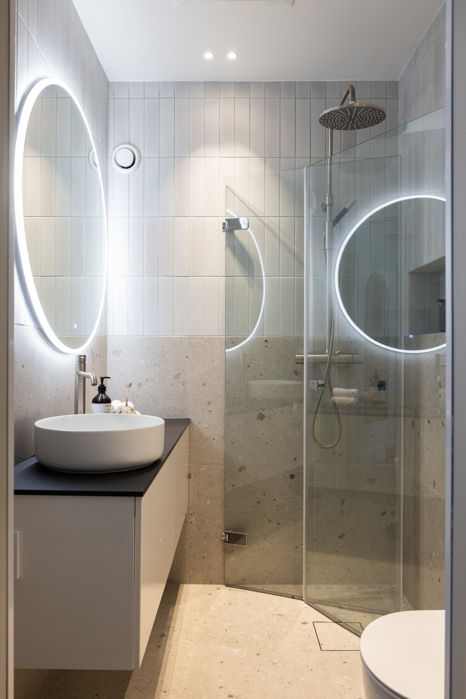 Delikat baderom som består av dusjhjørne, vegghengt toalett, servant over innredning og speil. Galleribilde