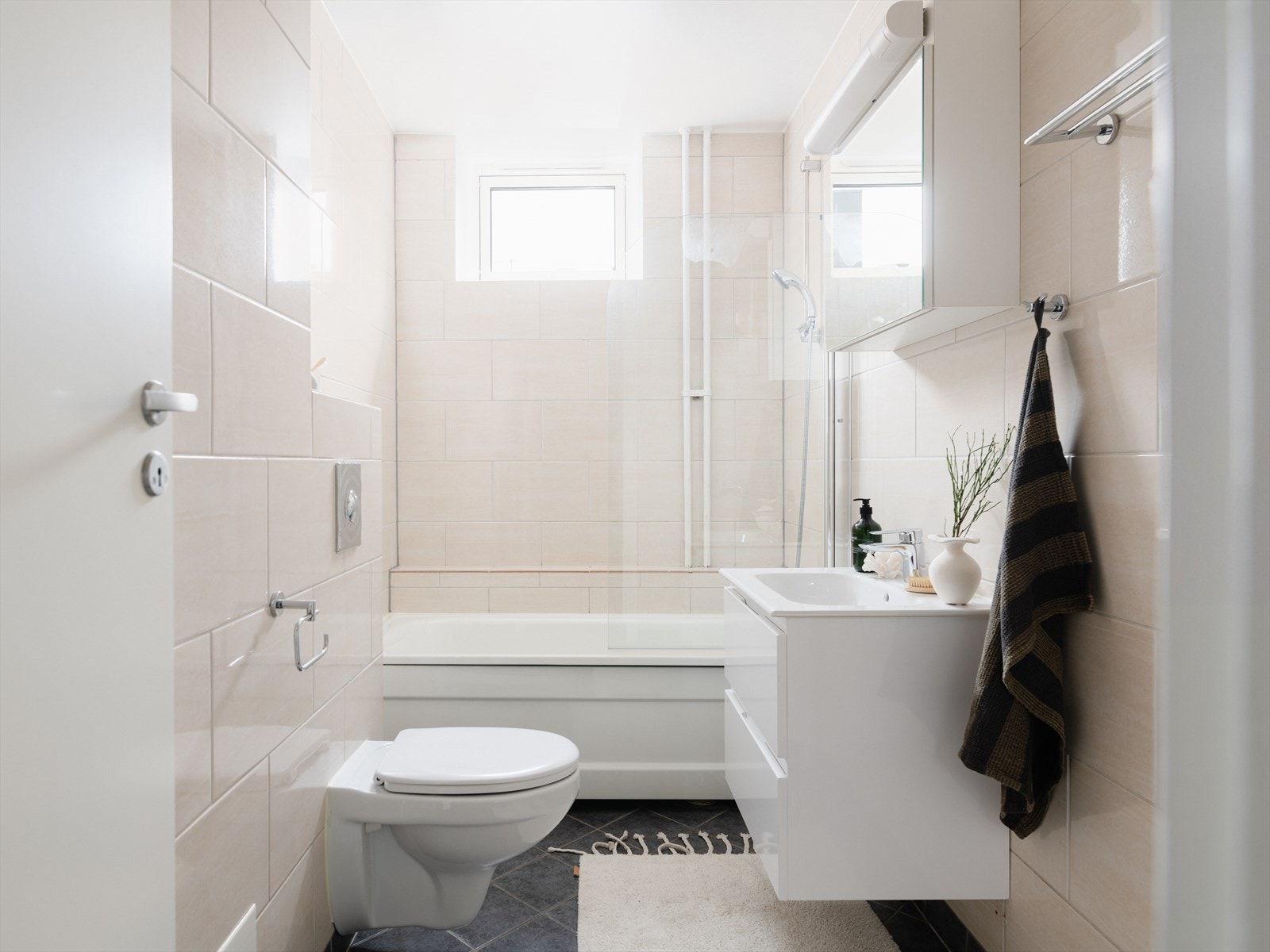 Badet er tidløst, med lyse fliser på vegger og mørke på gulv. Galleribilde