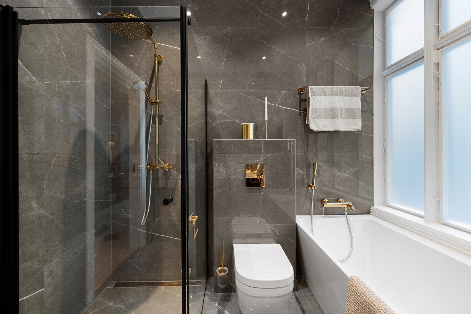 Her er det blandebatterier og detaljer i fargen Cool sunrise, store, grå fliser på veggene og matchende fliser på gulv med behagelig gulvvarme. Galleribilde