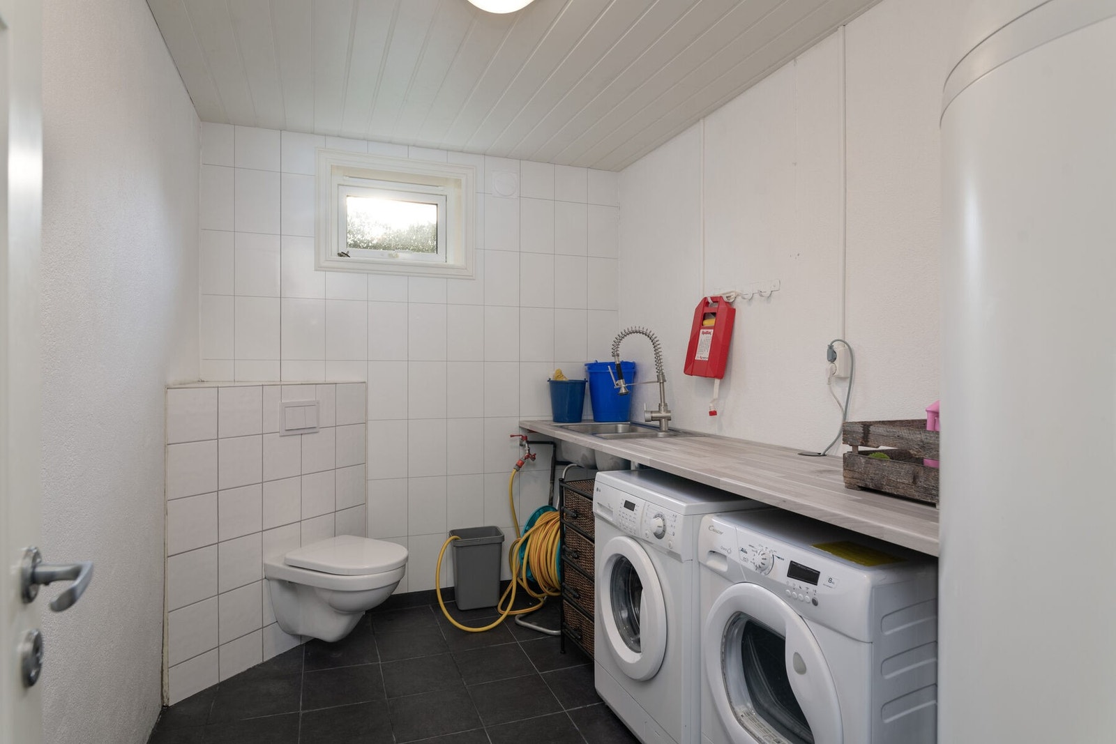 Separat vaskerom med opplegg for vaskemaskin, toalett og skyllekar nedfelt i benkeplate. Rommet har varmekabler i gulvet. Galleribilde