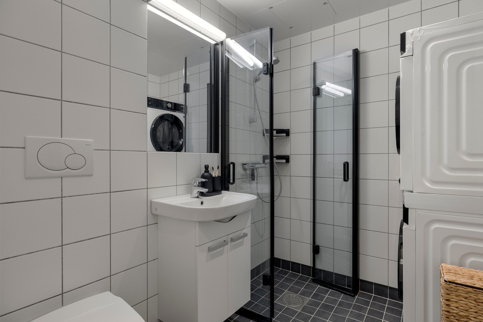 Badet inneholder servant, vegghengt toalett, dusjhjørne med foldbare dører og opplegg for vaskemaskin/tørketrommel. Galleribilde