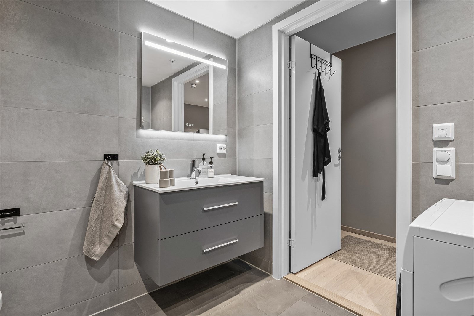 Badet er innredet med vegghengt klosett, servant med innredning, speil med lys og dusjhjørne med svingbare glassdører. Det er opplegg for vaskemaskin og gulvvarme på baderommet. Galleribilde