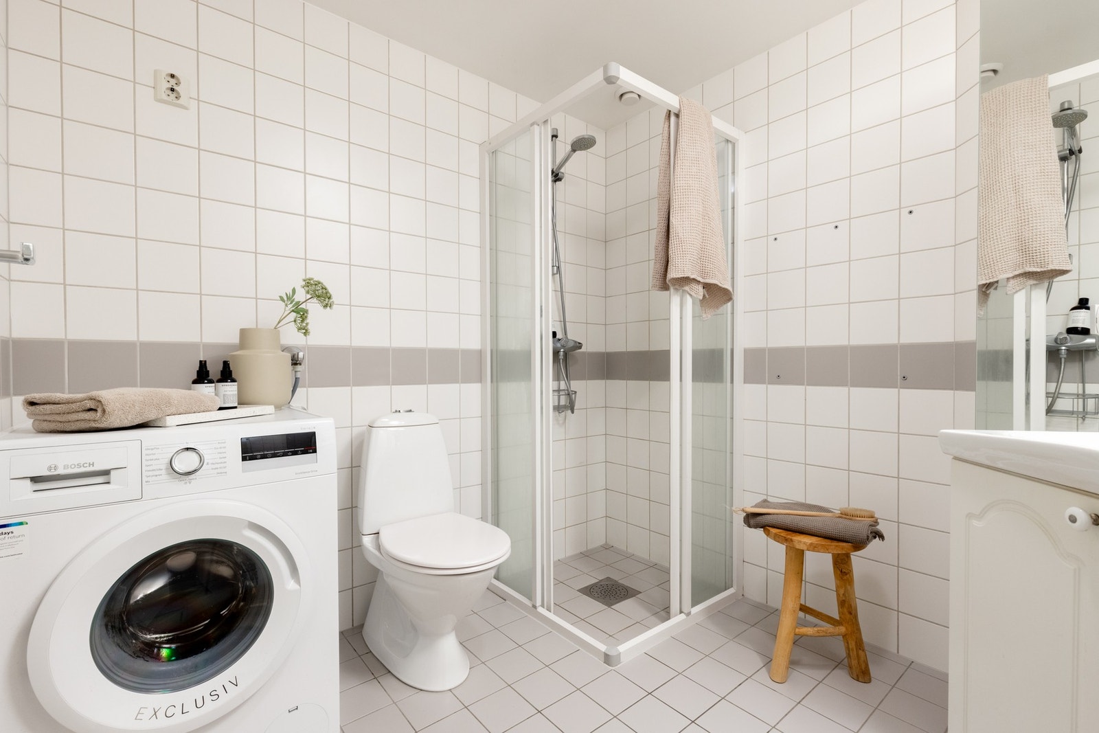 Innredningen består av servant på underskap, vegghengt speil med overbelysning, gulvstående toalett og dusjhjørne. Galleribilde