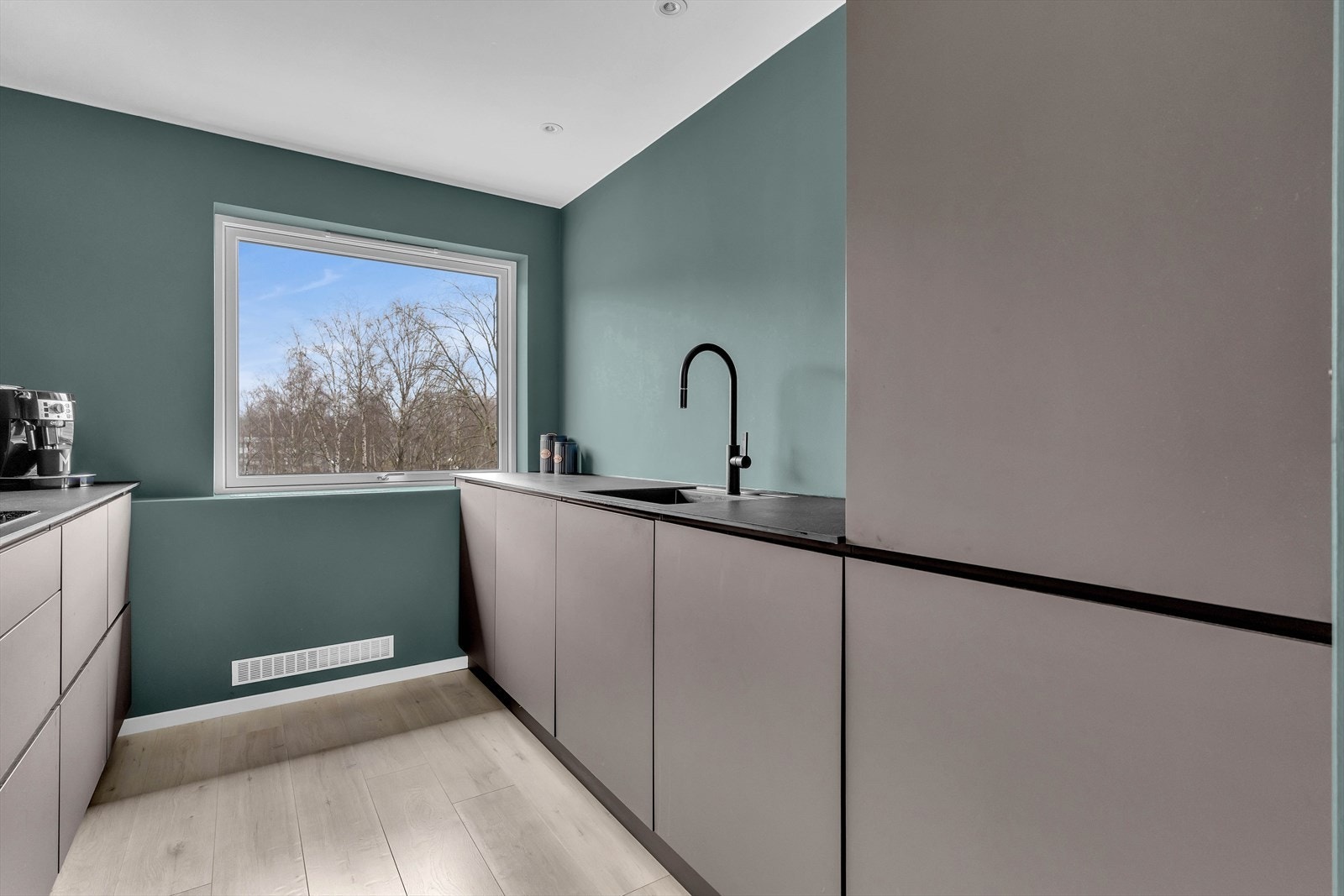 Et stort vindu sørger for rikelig med naturlig lysinnslipp, og de slette, grå flatene gir kjøkkenet et moderne og tidløst uttrykk. Galleribilde