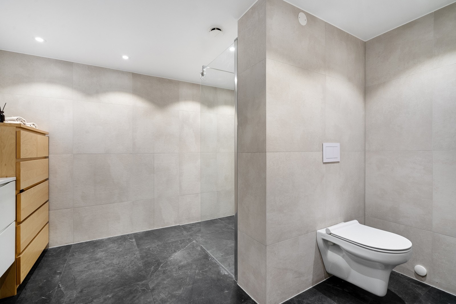 Badet er flislagt med gulvvarme, har nedsenket himling med downlights og vegghengt toalett. Vannrør av typen rør-i-rør system. Galleribilde