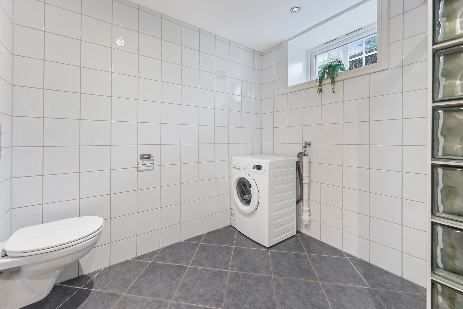 Badet er innredet med baderomsinnredning med nedfelt servant, vegghengt toalett, dusjvegger og opplegg for vaskemaskin Galleribilde