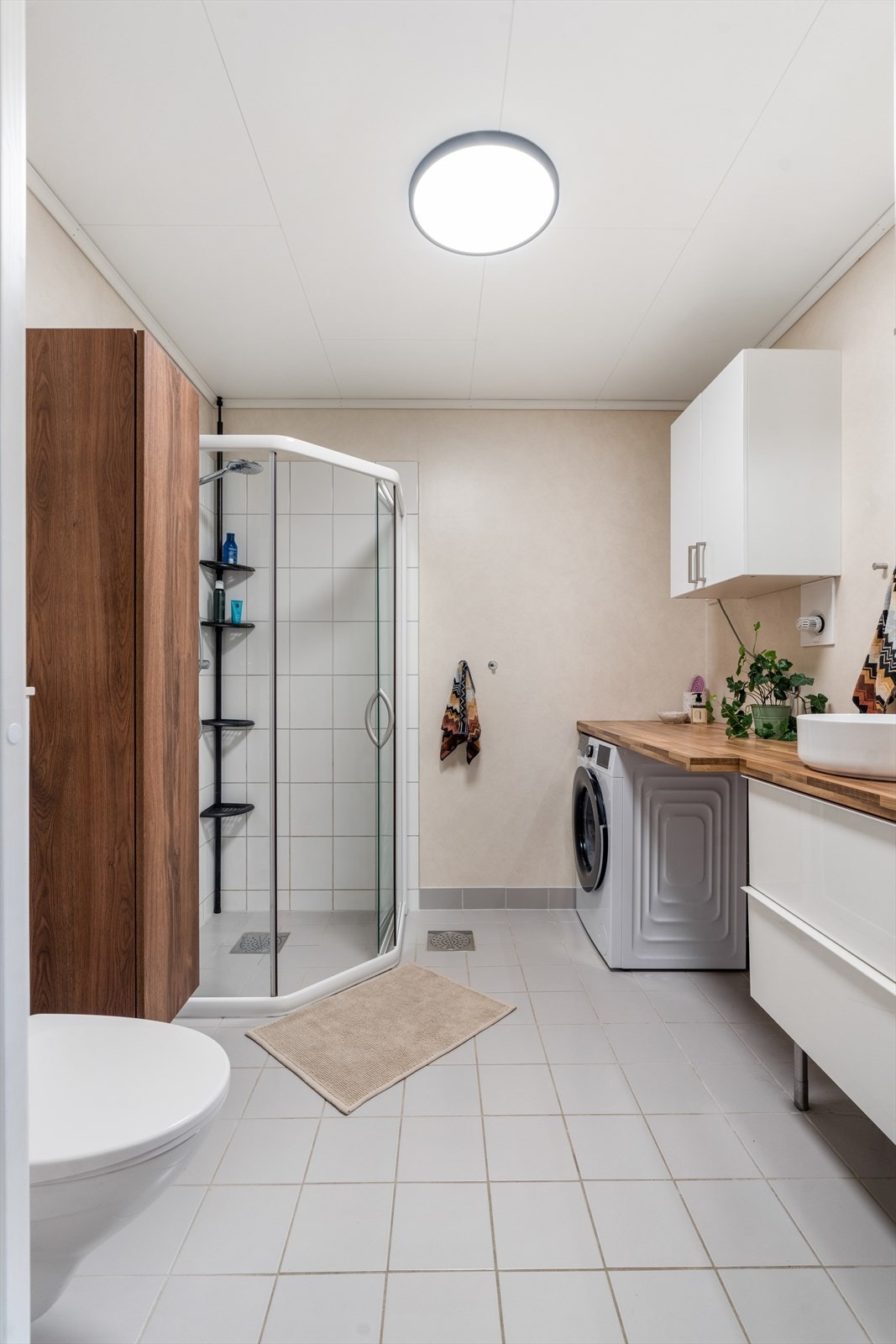 Pent bad med fliser på gulv og i dusjsonen. Praktisk vaskeromsløsning med god benkeplass. Galleribilde