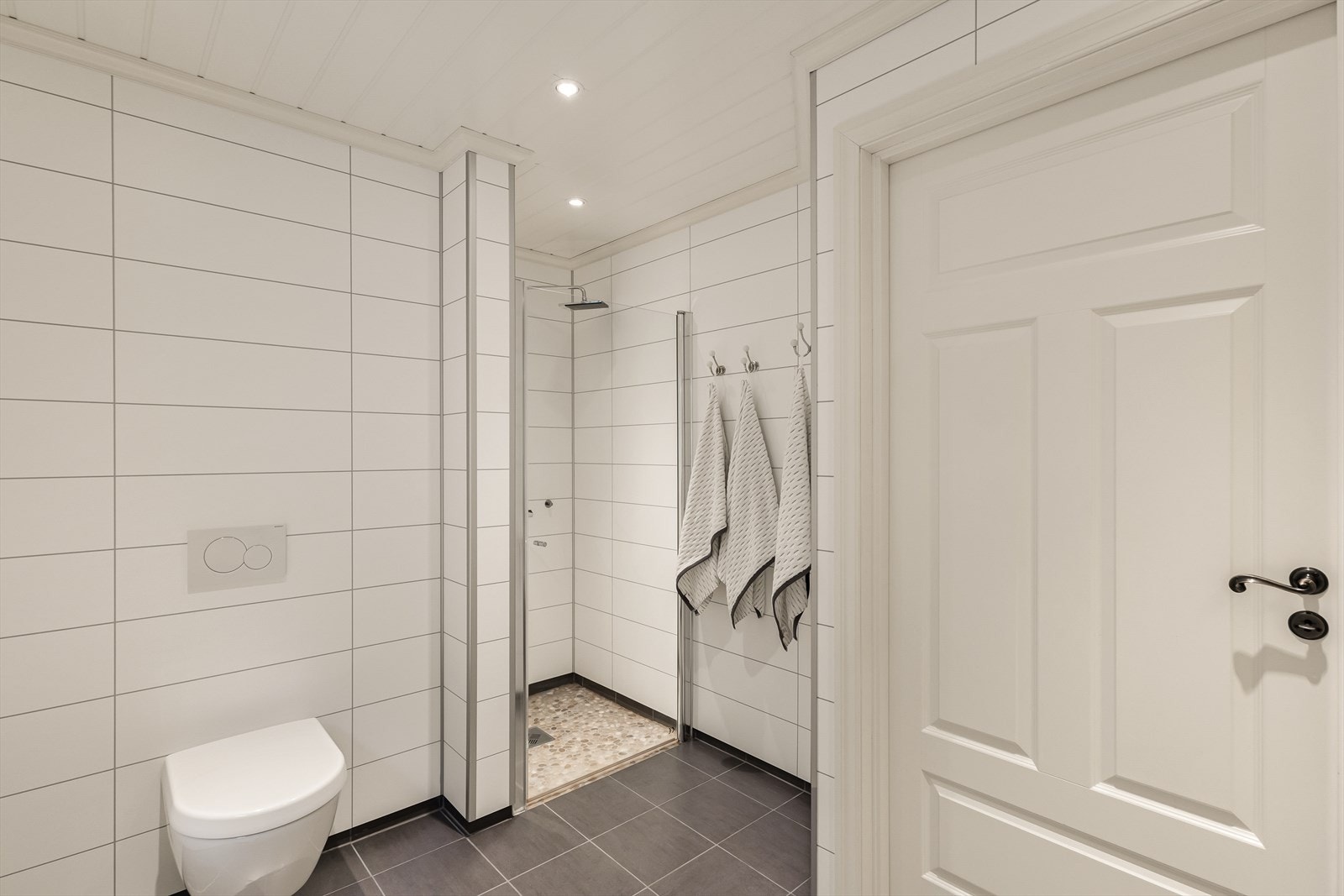 Det har varmekabler i gulvet og inneholder vegghengt toalett, dusjnisje og baderomsmøblement med servant. Galleribilde