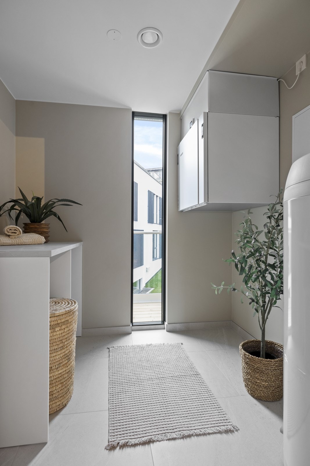 Praktisk og funksjonelt vaskerom med flislagt gulv, perfekt tilrettelagt for hverdagslivets behov. God benkeplass for sortering og bretting av klær. Med naturlig lysinnslipp fra vinduet, skapes en lys og innbydende følelse. Galleribilde