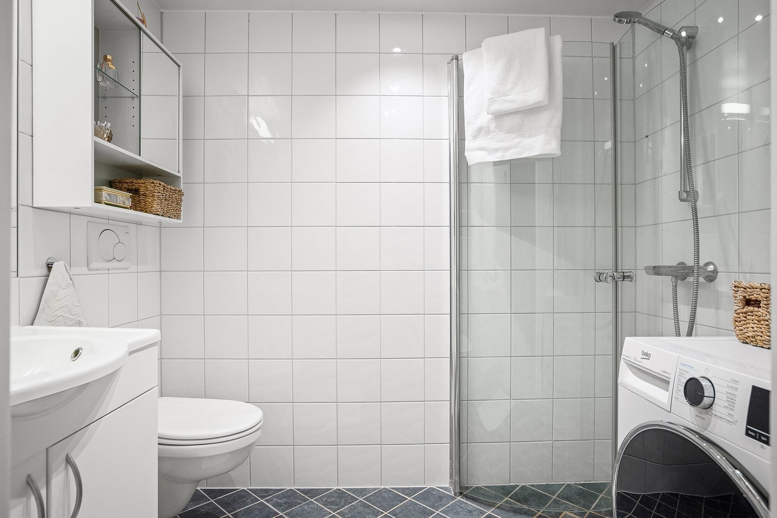 Pent baderom bestående av baderomsinnredning med glatte fronter og en heldekkende servant med innfelt speil og lysarmatur over. Galleribilde