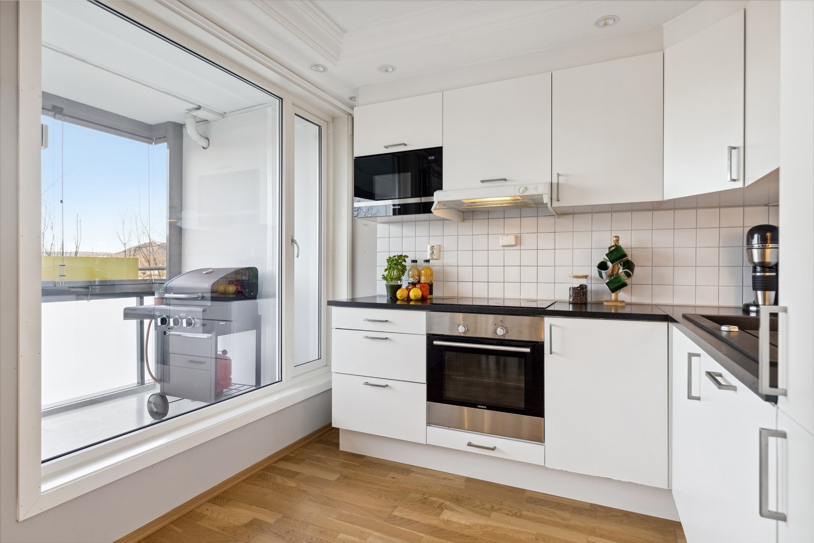 Meget lyst og hyggelig kjøkken med takhøy innredning og fliser over benken Galleribilde