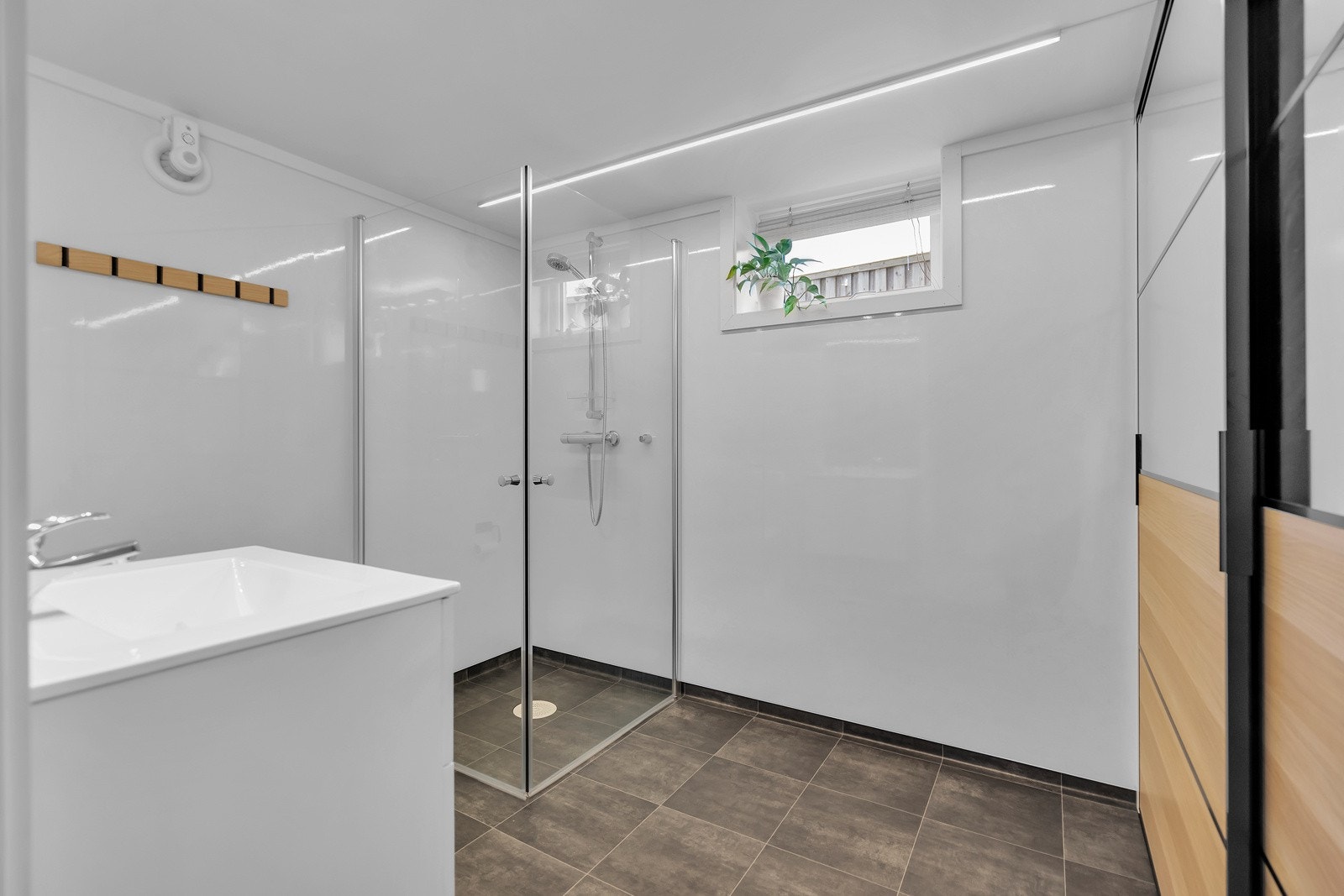 Bad/vaskrom med fliser på gulv. Innredet med dusj, wc, servantskap og vaksemaskin med skyvedør for å holde rommet ryddig. Galleribilde