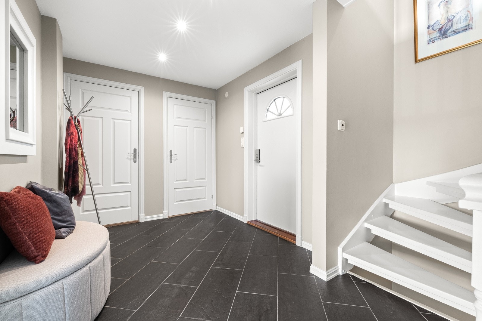 Inn i boligen ønskes du velkommen i en stor og delikat entré med flislagt gulv med vannbåren varme og slette vegger malt i en dus beige tone som står i flott kontrast til det mørkere gulvet. Galleribilde