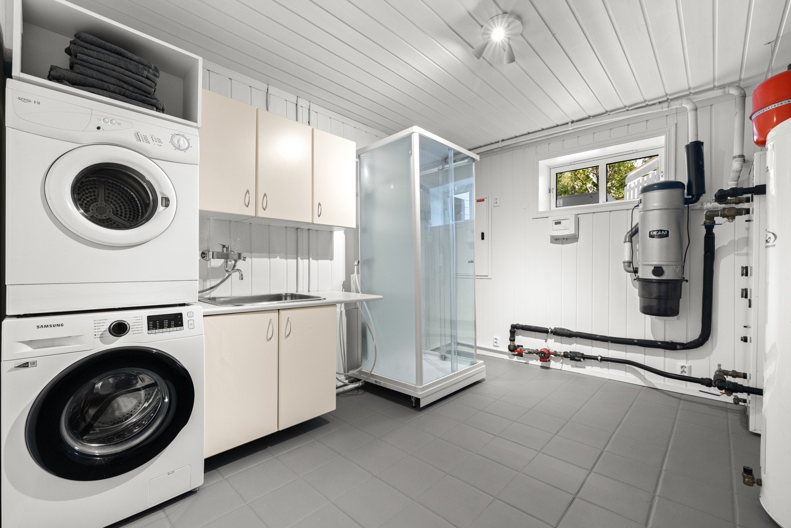 Baderommet i kjelleren er kombinert vaskerom og har fliser på gulv med gulvvarme, malte panelvegger og malt himling. Galleribilde