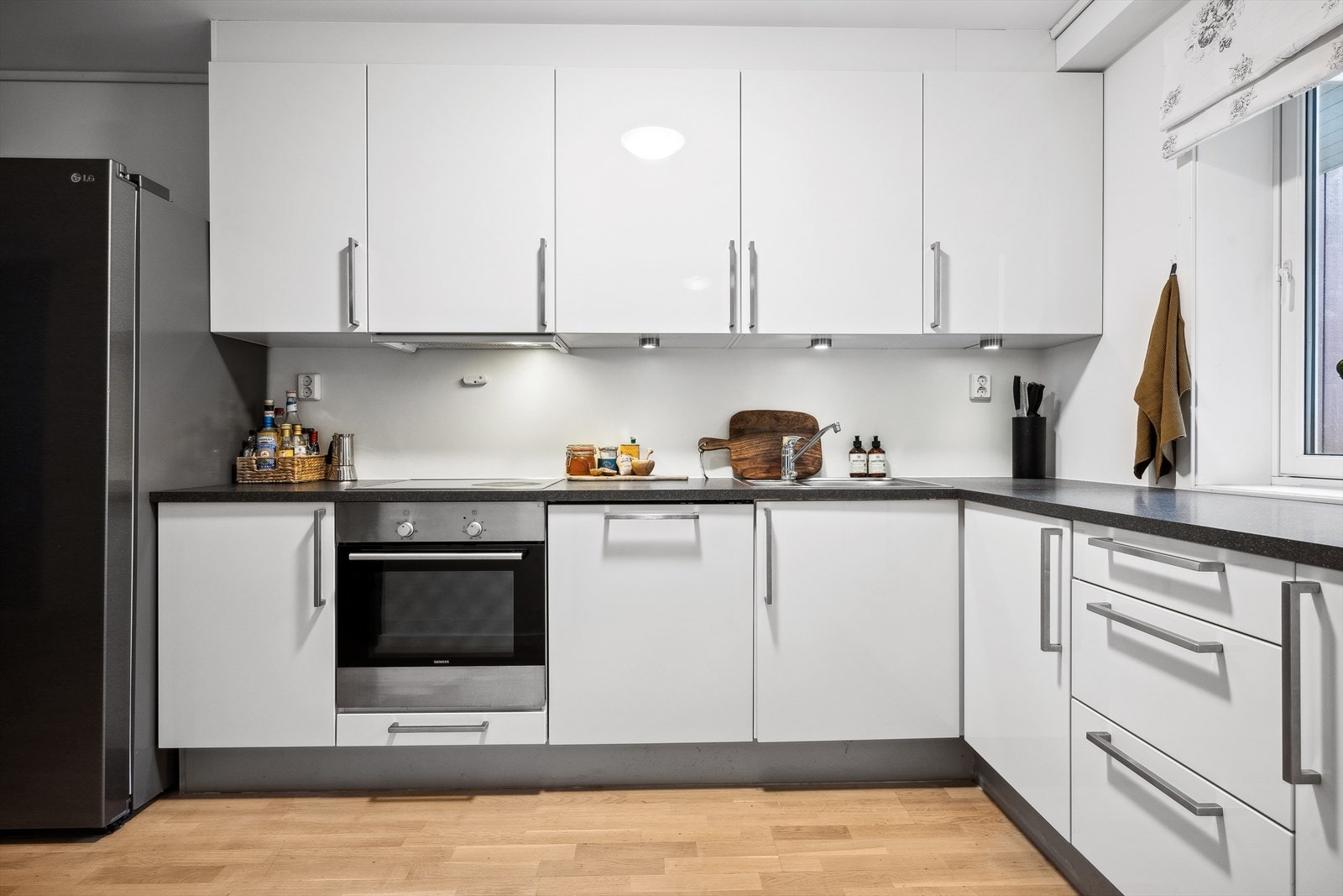 Kjøkken med hvite glatte fronter og laminat benkeplate med nedfelt servant og spotter under overskap. Galleribilde