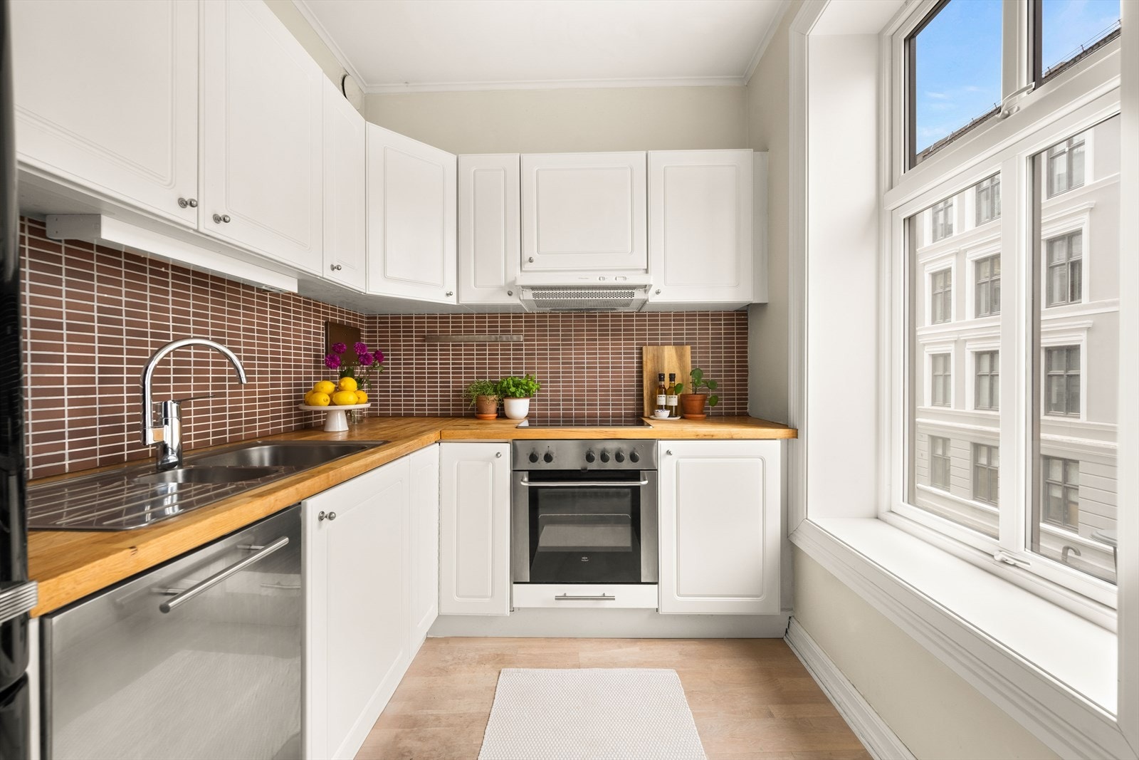 Lys innredning med profilerte fronter, fliser på vegg over kjøkkenbenken og heltre benkeplate. Galleribilde