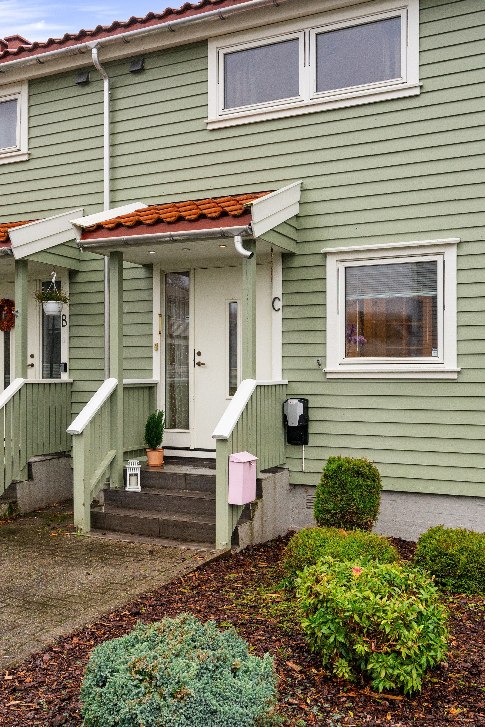 Inngangsparti. El-bil lader på husveggen. Det er parkering i garasje. Galleribilde