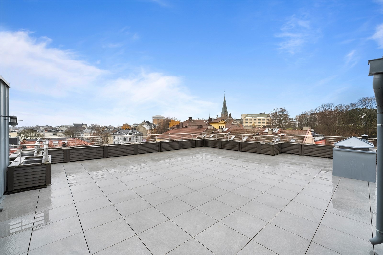 Stor takterrasse med strålende solforhold og nydelig utsikt over byens tak. Galleribilde