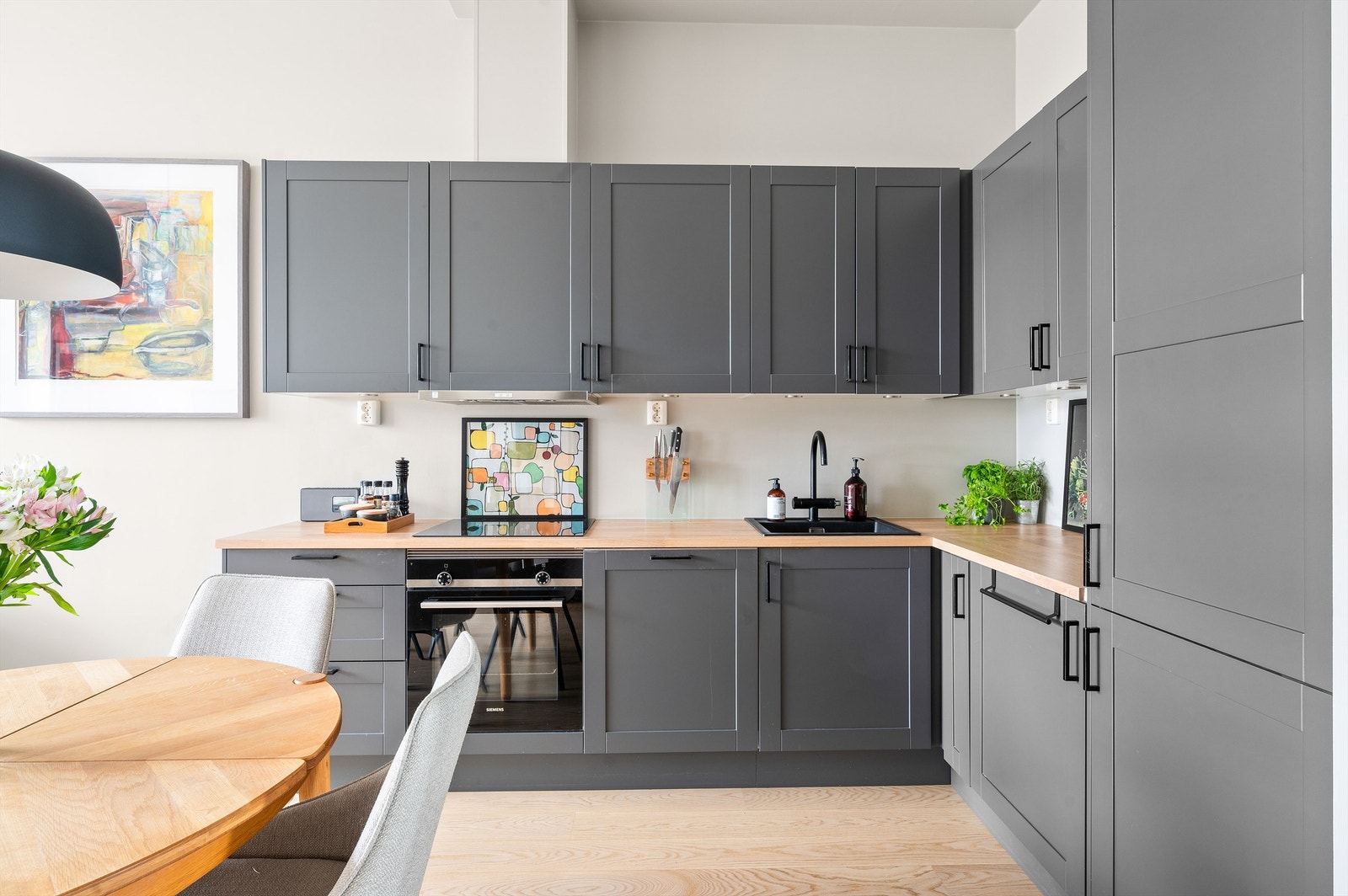 Kjøkkeninnredning med mørke, profilerte skapfronter, benkeplater i tre, nedfelt rustfri oppvaskkum og ett-greps armatur Galleribilde