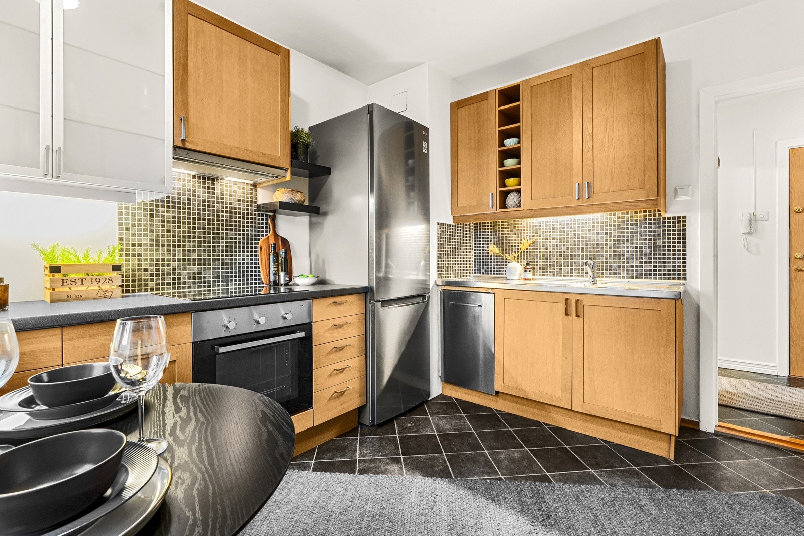 Enkelte overskap med vitrinefronter med frostet glass gir et mykere inntrykk. Integrert induksjonsplatetopp, stekeovn og oppvaskmaskin (smal type), samt frittstående kjøleskap medfølger i handelen. Galleribilde