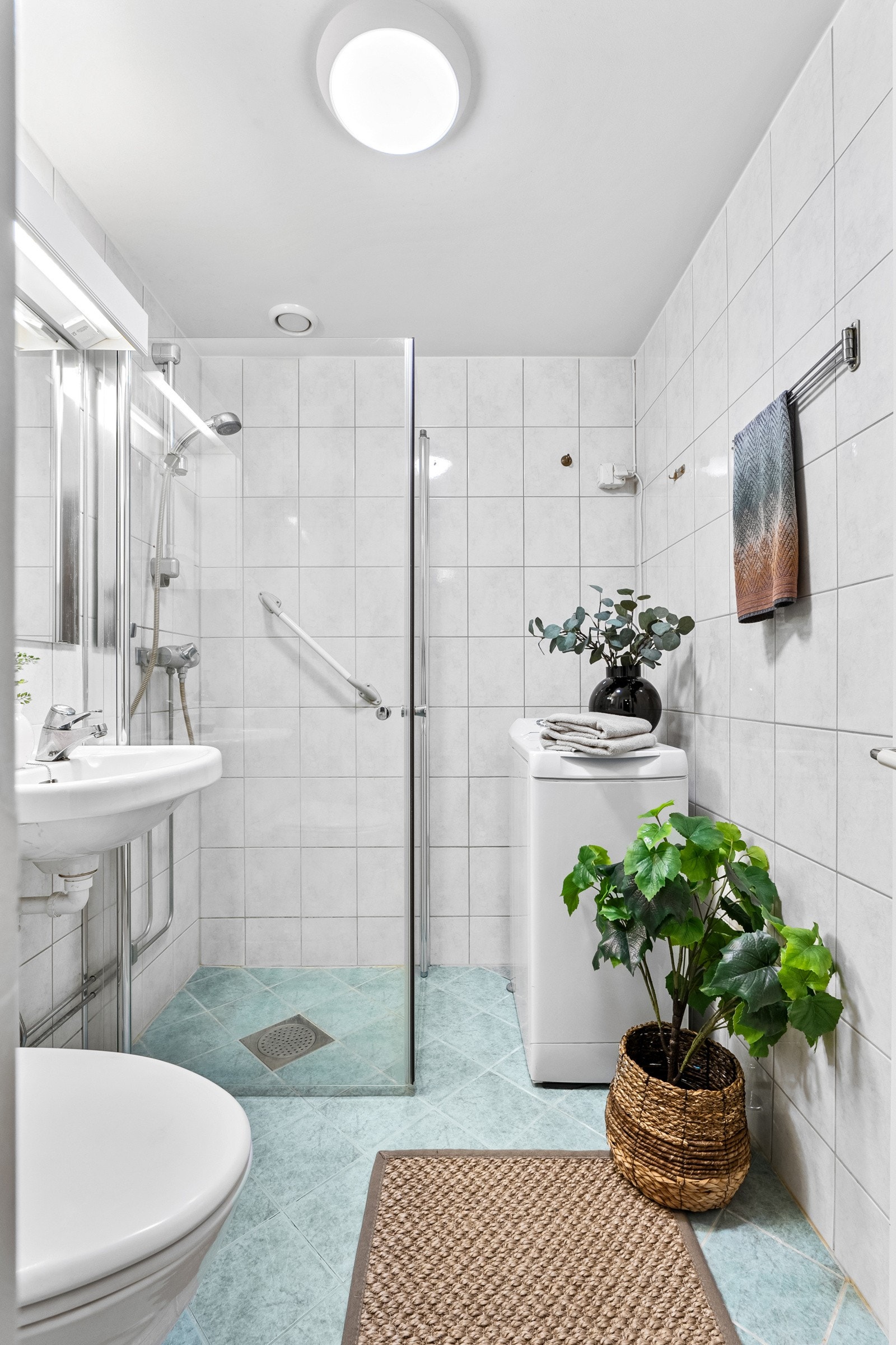 Egen dusjsone med innfellbare glassdører, sluk og termostatstyrt blandebatteri. Videre er badet utstyrt med gulvmontert klosett, servant montert på vegg og speil med lysarmatur. Vaskemaskinen medfølger i handelen. Galleribilde