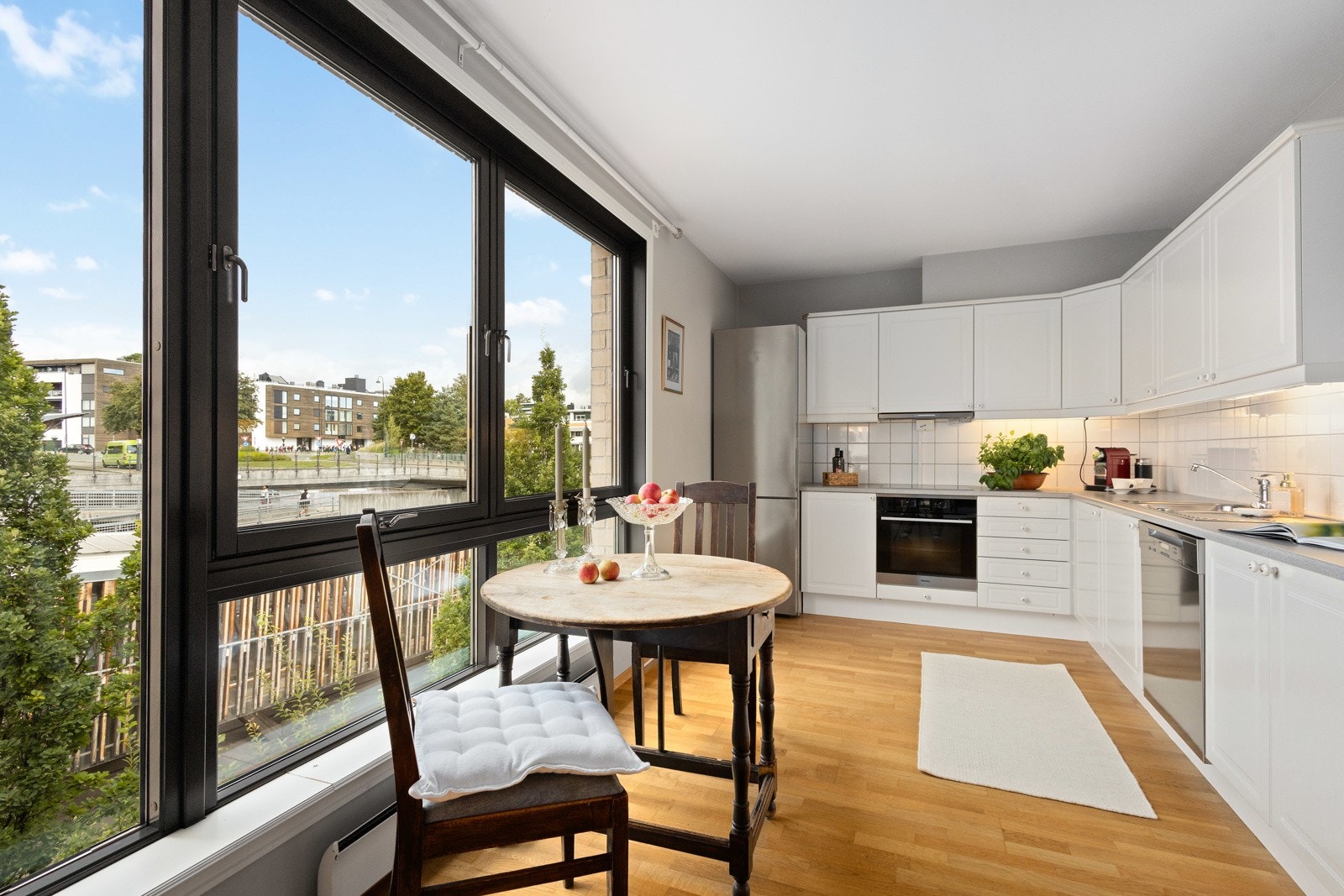 Hyggelig kjøkken med hvit kjøkkeninnredning og integrerte hvitevarer som stekeovn, platetopp og oppvaskmaskin. Galleribilde