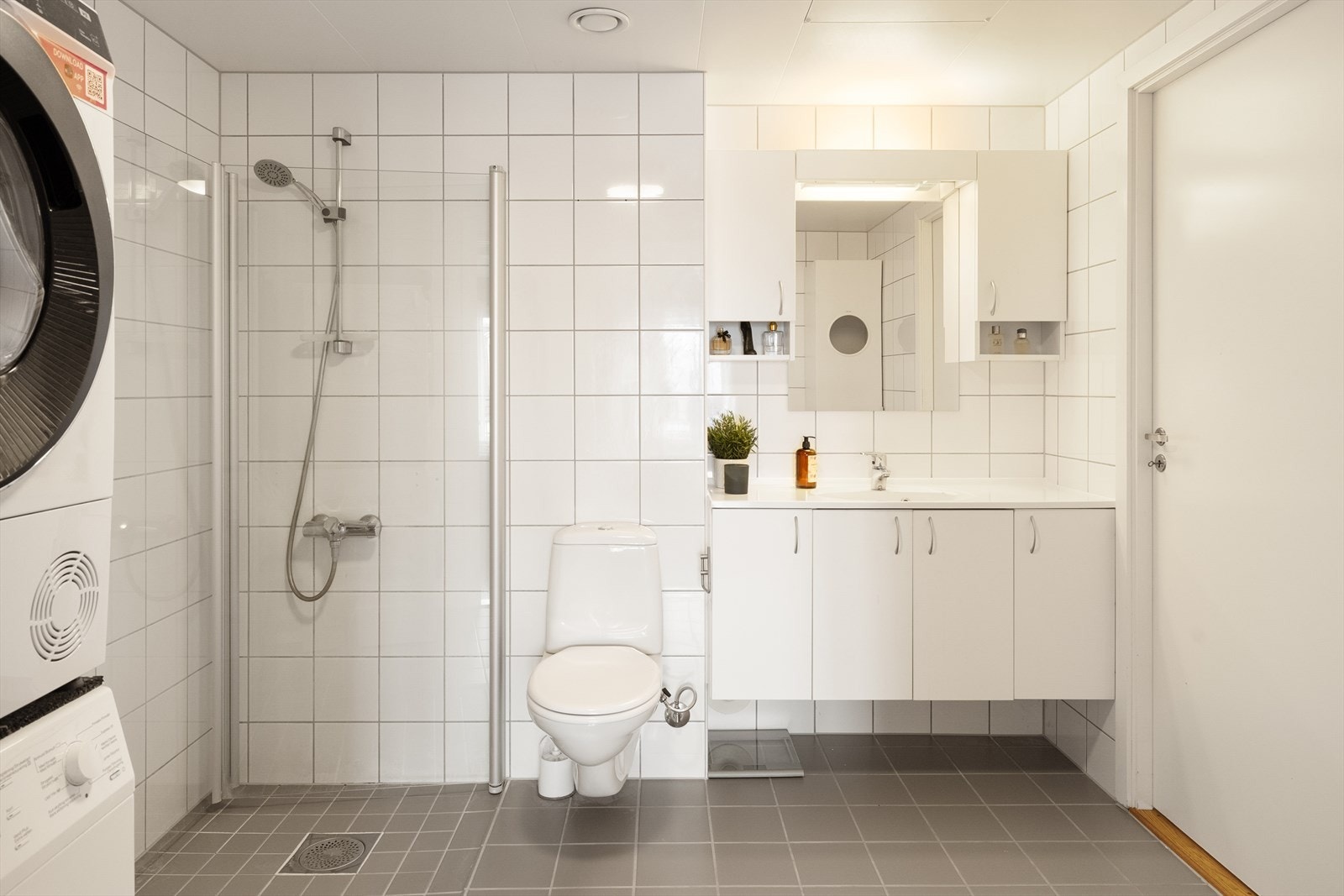 Badet er utstyrt med vegghengt klosett, servant nedfelt i innredning, speil, og et dusjhjørne med svingbare glassdører. Galleribilde