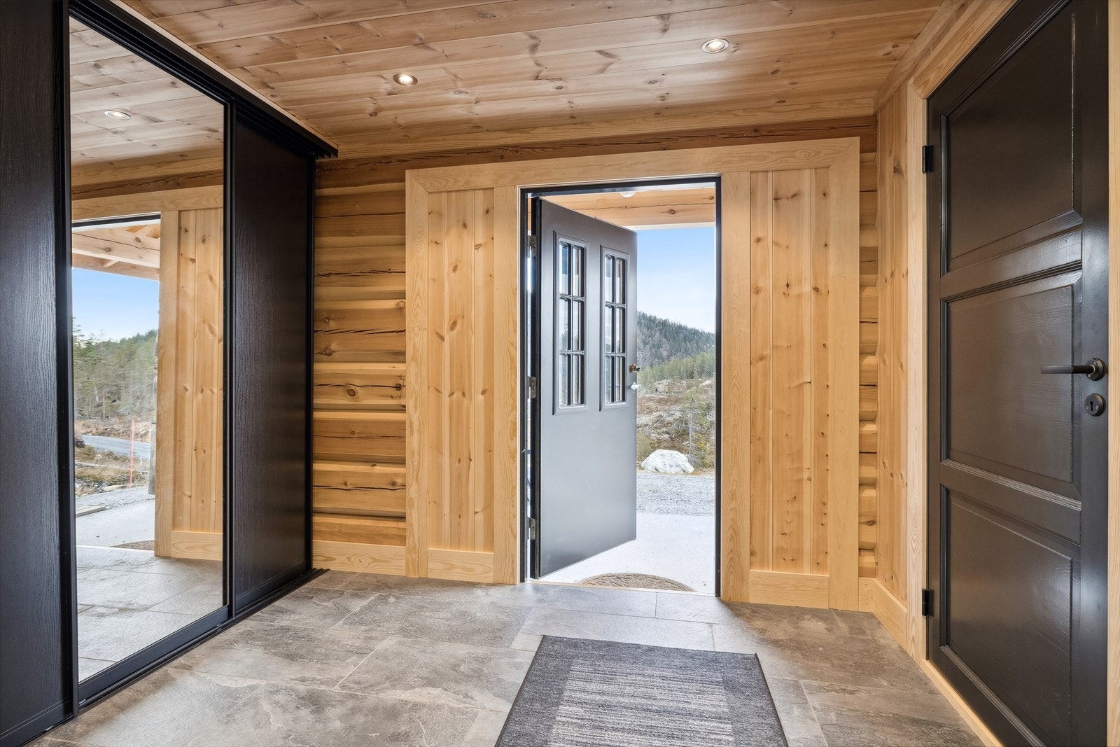 Vindfang med elektriske varmekabler i flislagt gulv og LED-spot i tak. Det er god plass for oppheng av yttertøy i en romslig skyvedørsgarderobe. Galleribilde