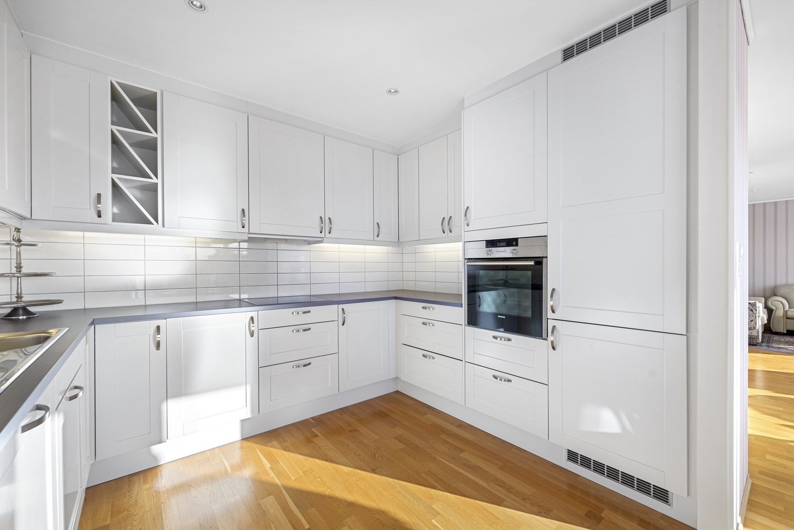 Integrerte hvitevarer (komfyr, oppvaskmaskin, induksjonstopp, kjøl-/fryseskap) samt fliser over kjøkkenbenk. Galleribilde