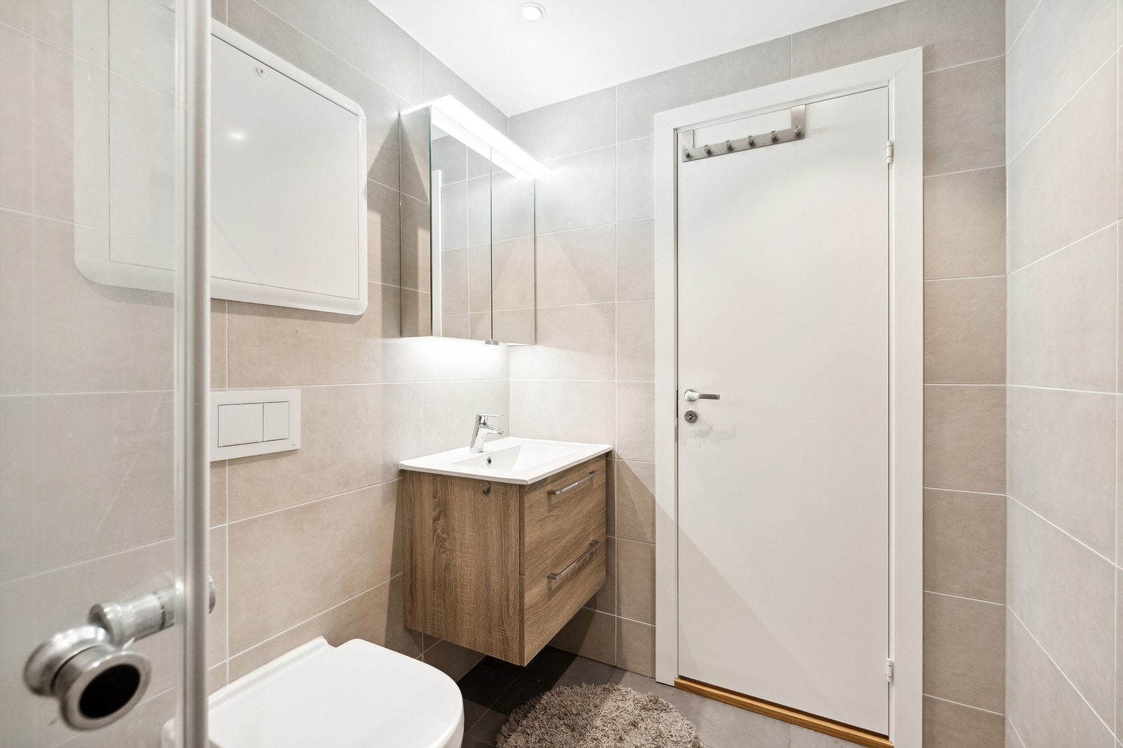 Badet er innredet med nedfelt servant i skuffeinnredning, speilskap, veggmontert toalett, dusjhjørne med dører og opplegg for vaskemaskin. Galleribilde