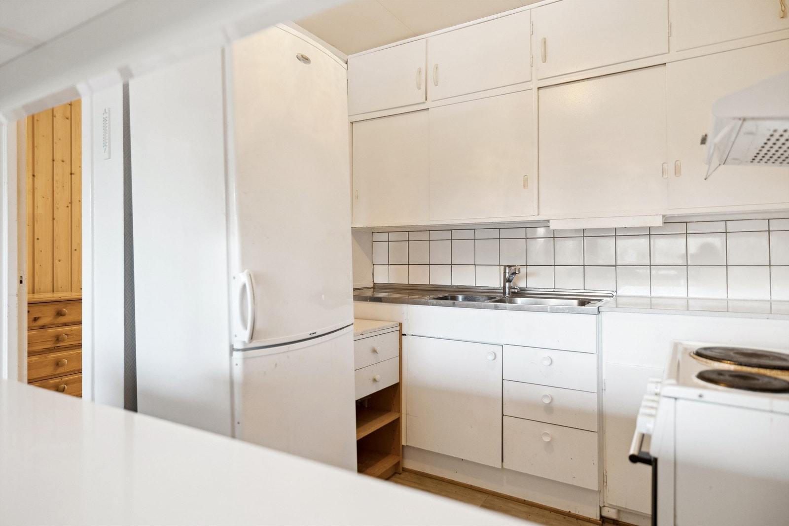 Kjøkkenet har laminat på gulvet. Lys innredning med glatte fronter. Fliser mellom benk og overskap. Galleribilde