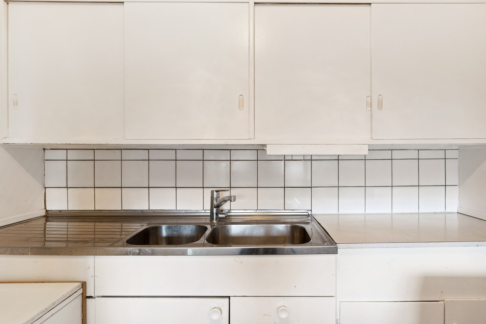 Dobbelt vaskekum i metall med benkebeslag. Innredningen består av overskap, underskap, skuffer og en innredningen mot stuen som romdeler. Galleribilde