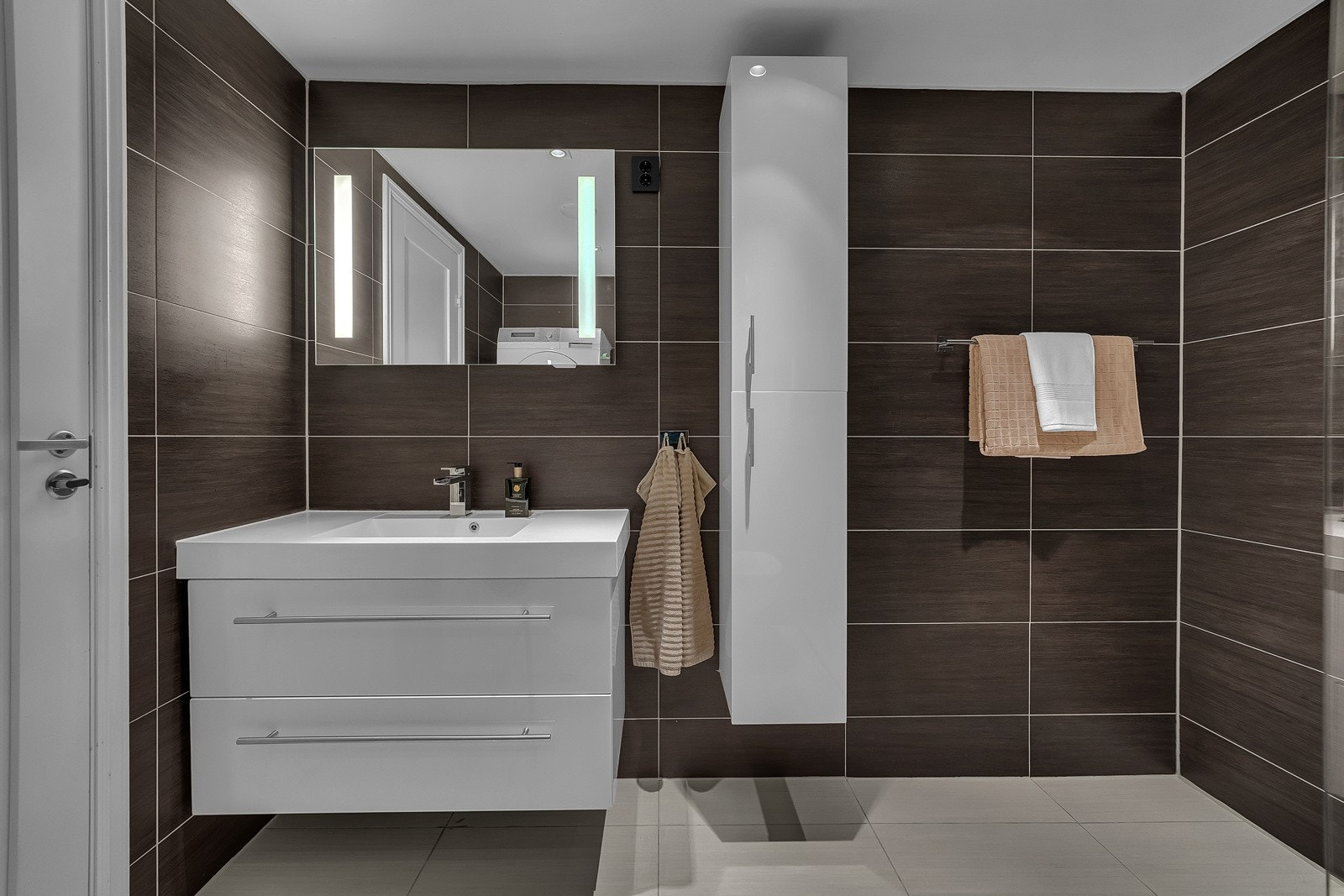 Baderomsinnredning består av benkeskap og veggskap med frostede glassfronter, veggskap med speilfronter, servant og belysning over servant. Galleribilde