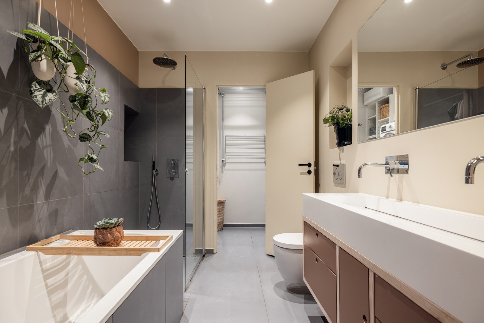 Innredningen består av en veggmontert servantskap med dobbelt armatur, et vegghengt toalett, badekar og en separat dusjnisje Galleribilde