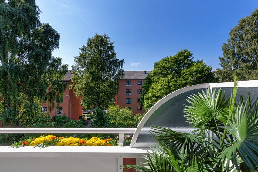Stuen og balkongen har et hyggelig, grønt utsyn på sommerstid og vender ut mot rolig sidegate (sommerbilde fra nabobalkong med samme utsyn). Galleribilde