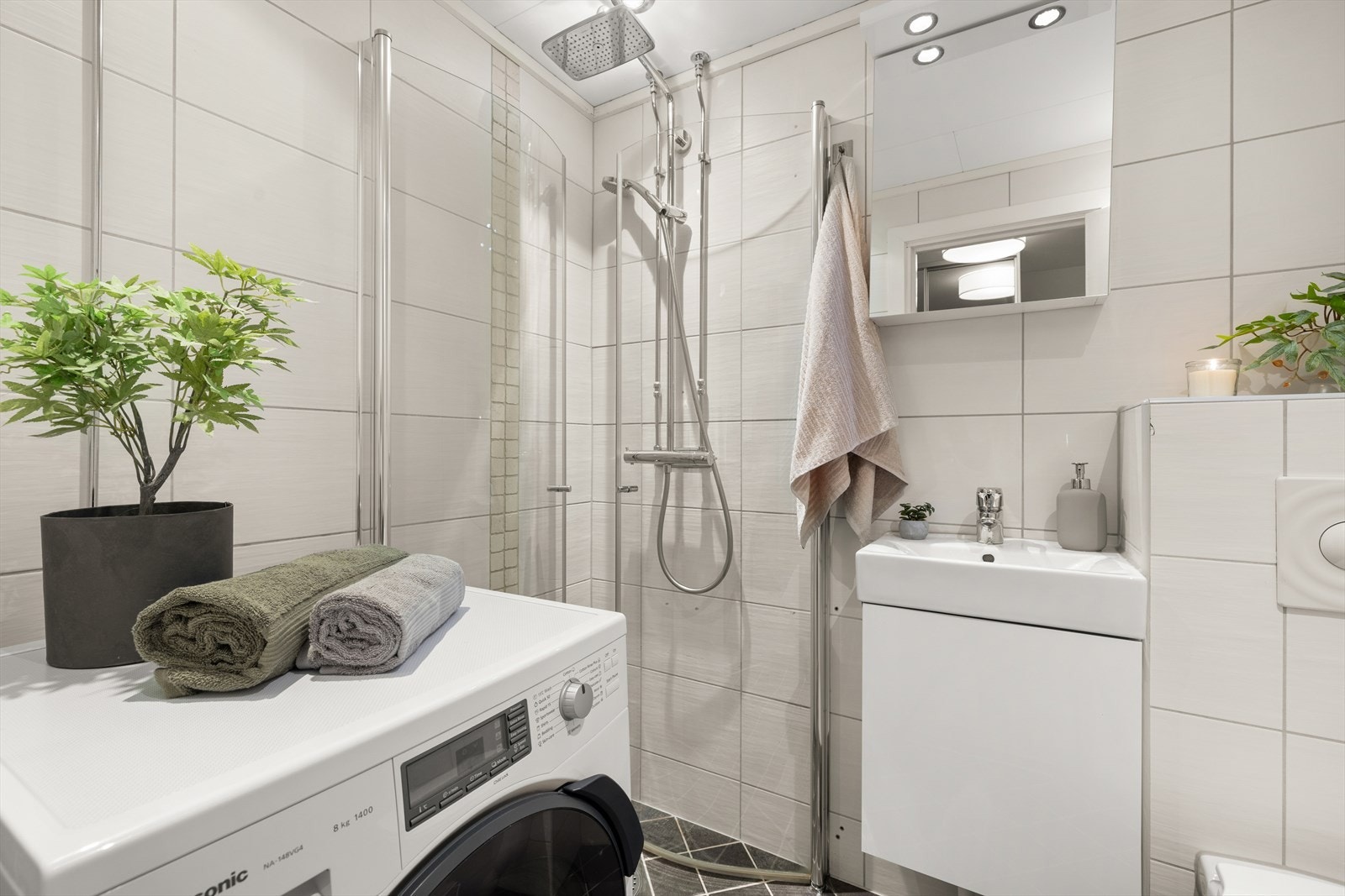 Badet har varmekabler på gulv, praktisk dusjhjørne, servant med oppbevaring og opplegg for vaskemaskin Galleribilde