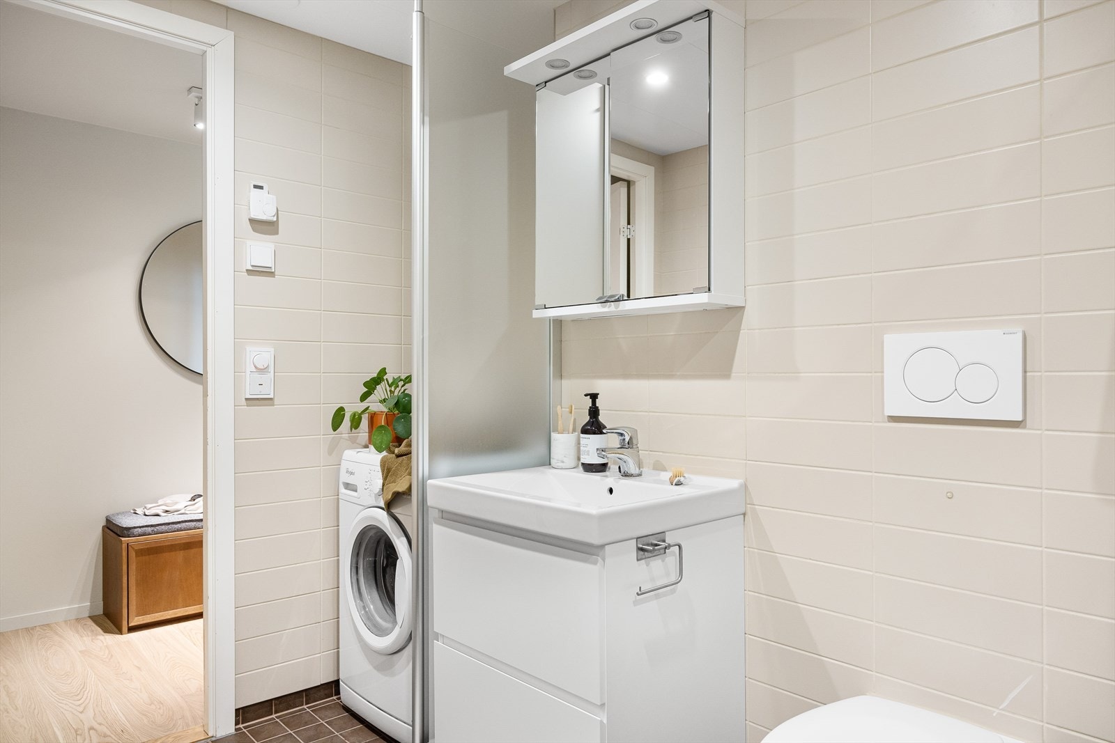 Badet er innredet med nedfelt servant, veggmontert toalett, dusjvegger i hjørnet, samt opplegg for vaskemaskin og tørketrommel. Galleribilde