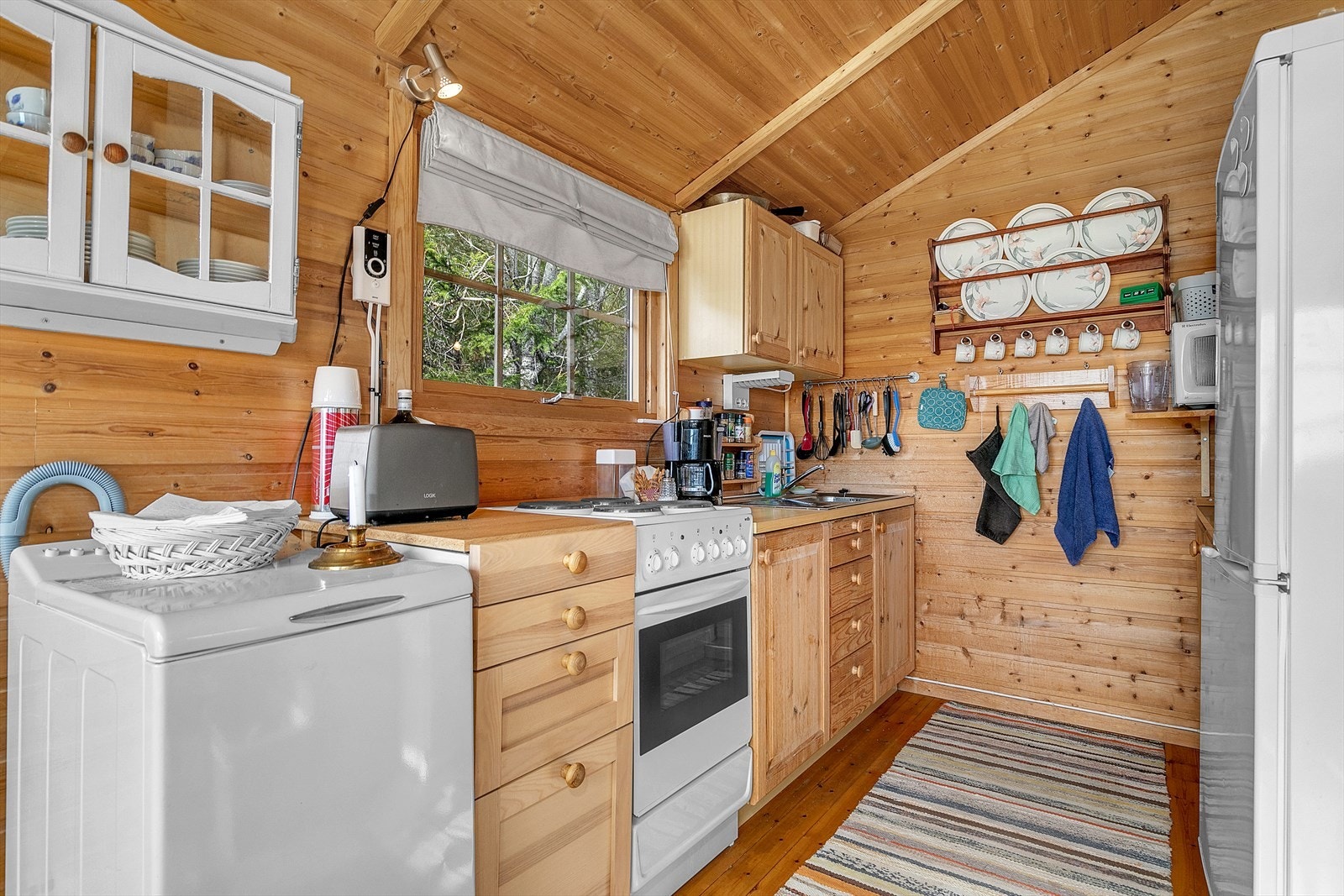 Kjøkkeninnredning av typen furukjøkken. Kjøkkenet inneholder også frittstående komfyr og kjøl- og fryseskap. Galleribilde