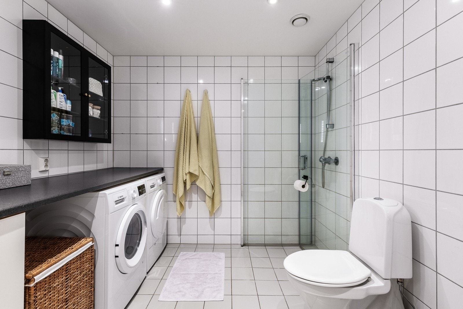 Under benken er det opplegg for plass for både vaskemaskin og tørketrommel, og badet er videre utstyrt med toalett og et dusjhjørne med innfellbare glassdører. Galleribilde